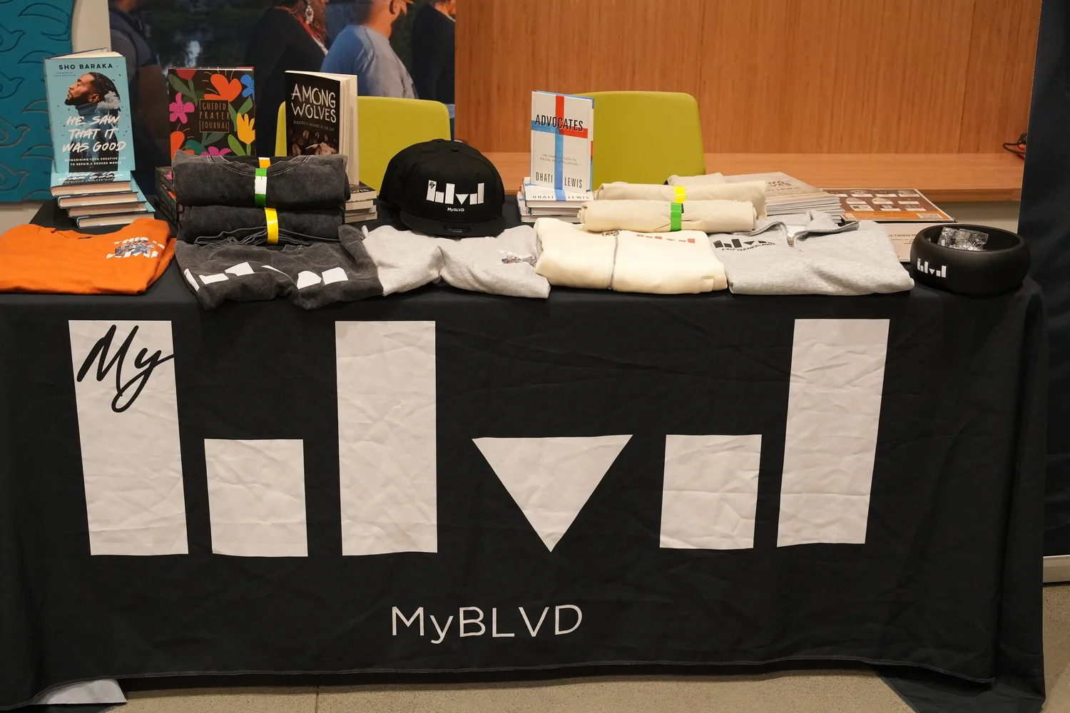 MyBLVD merchandise table with folded shirts, hats, and books.