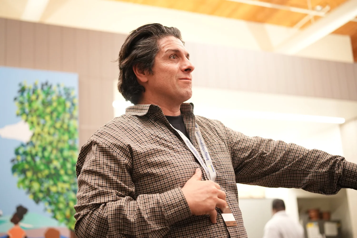 Speaker in a checked jacket extending an arm toward the room.