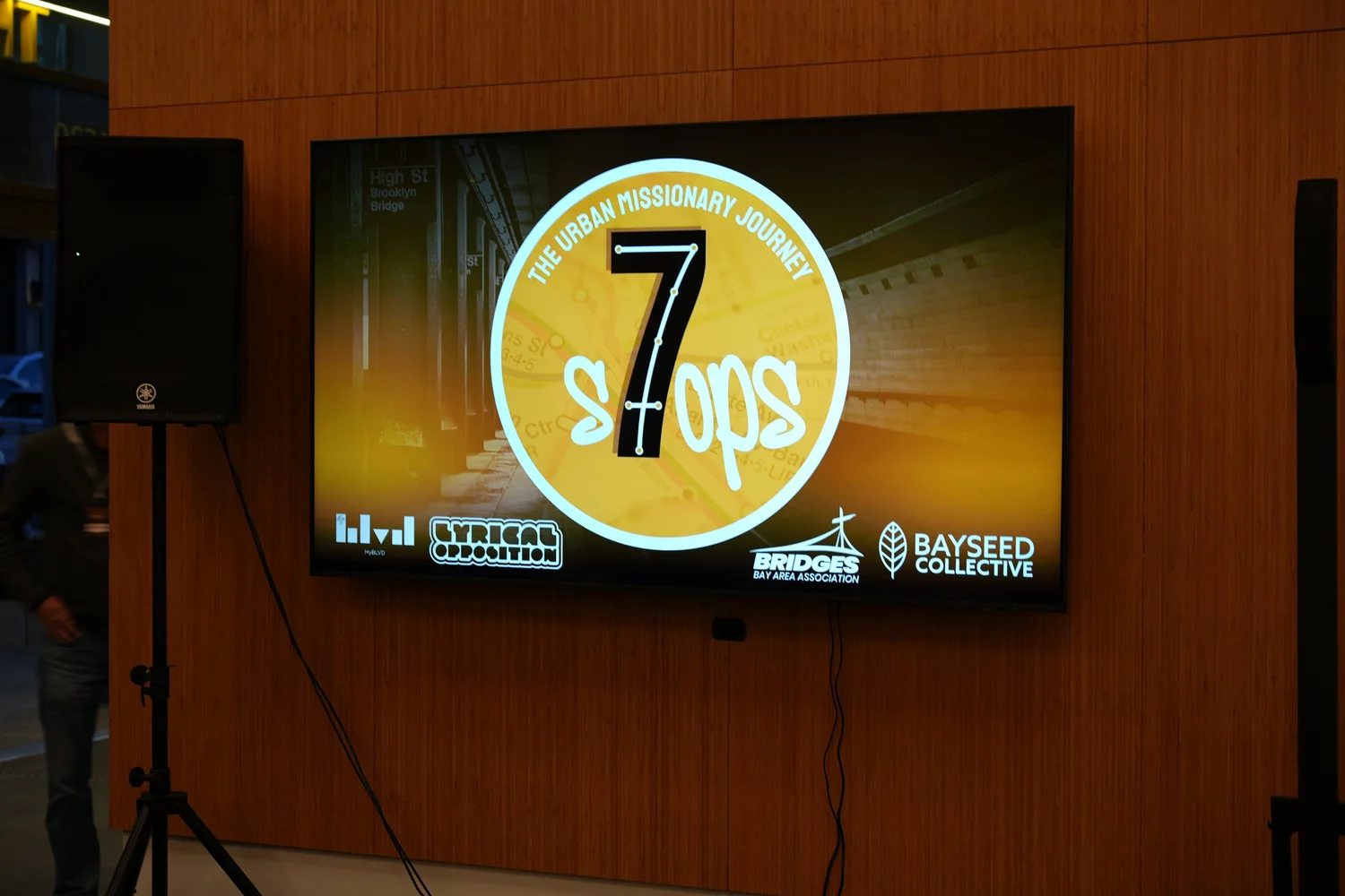 Seven Stops event graphic on a wall-mounted screen.