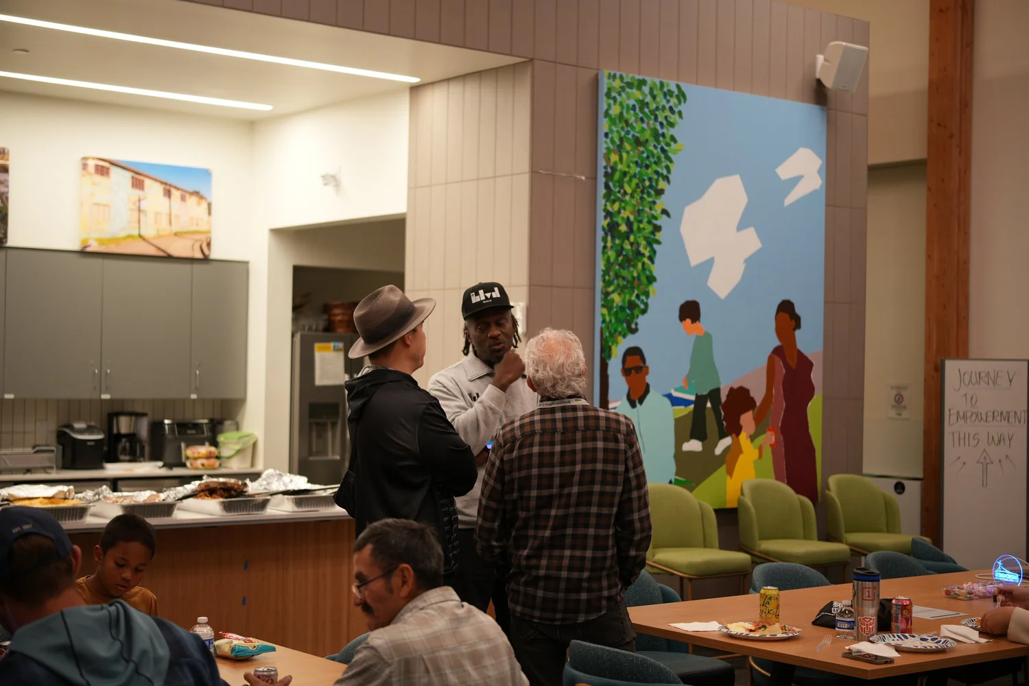 Guests talking near the kitchen and a colorful mural.