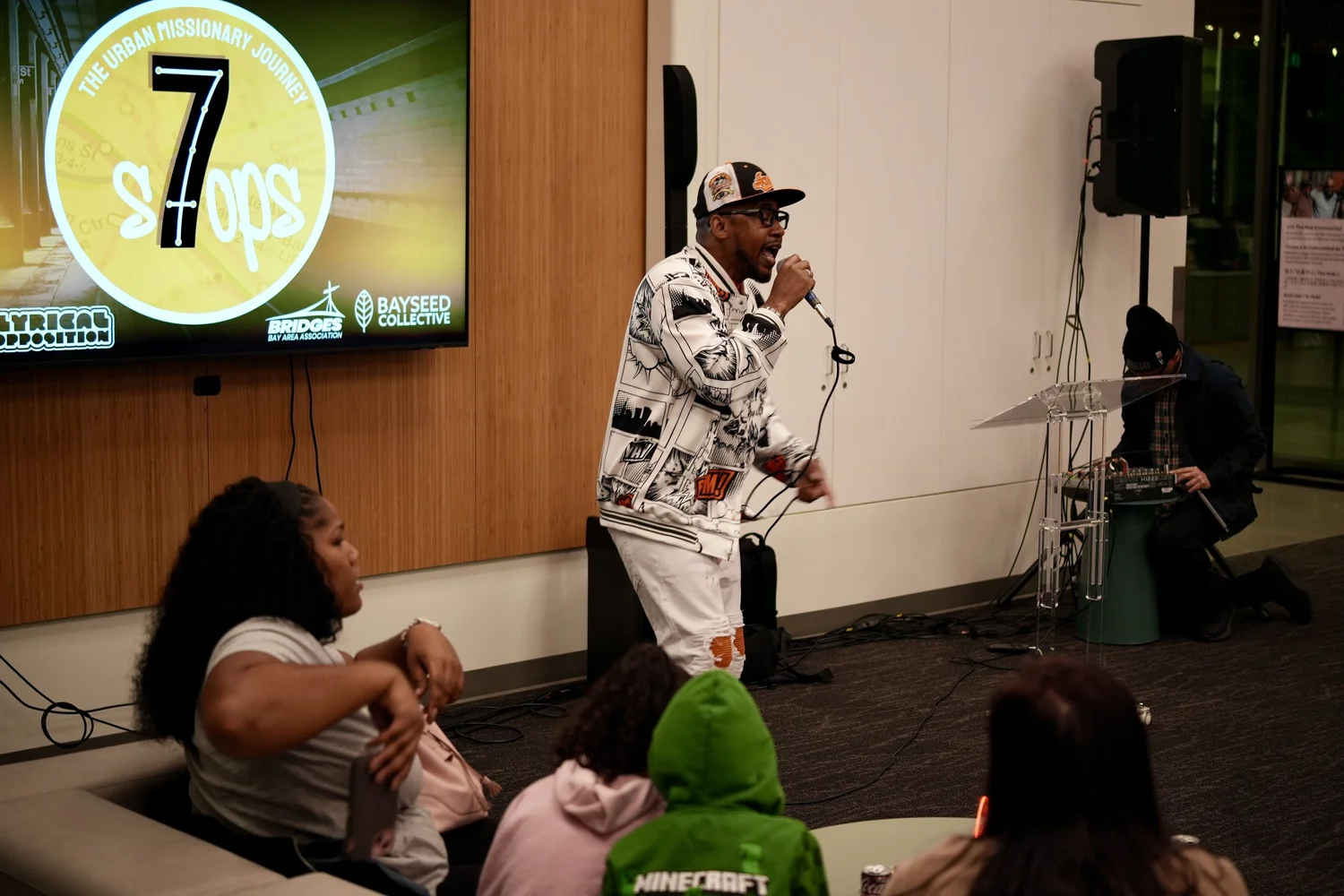 Performer in a patterned jacket addressing families seated nearby.