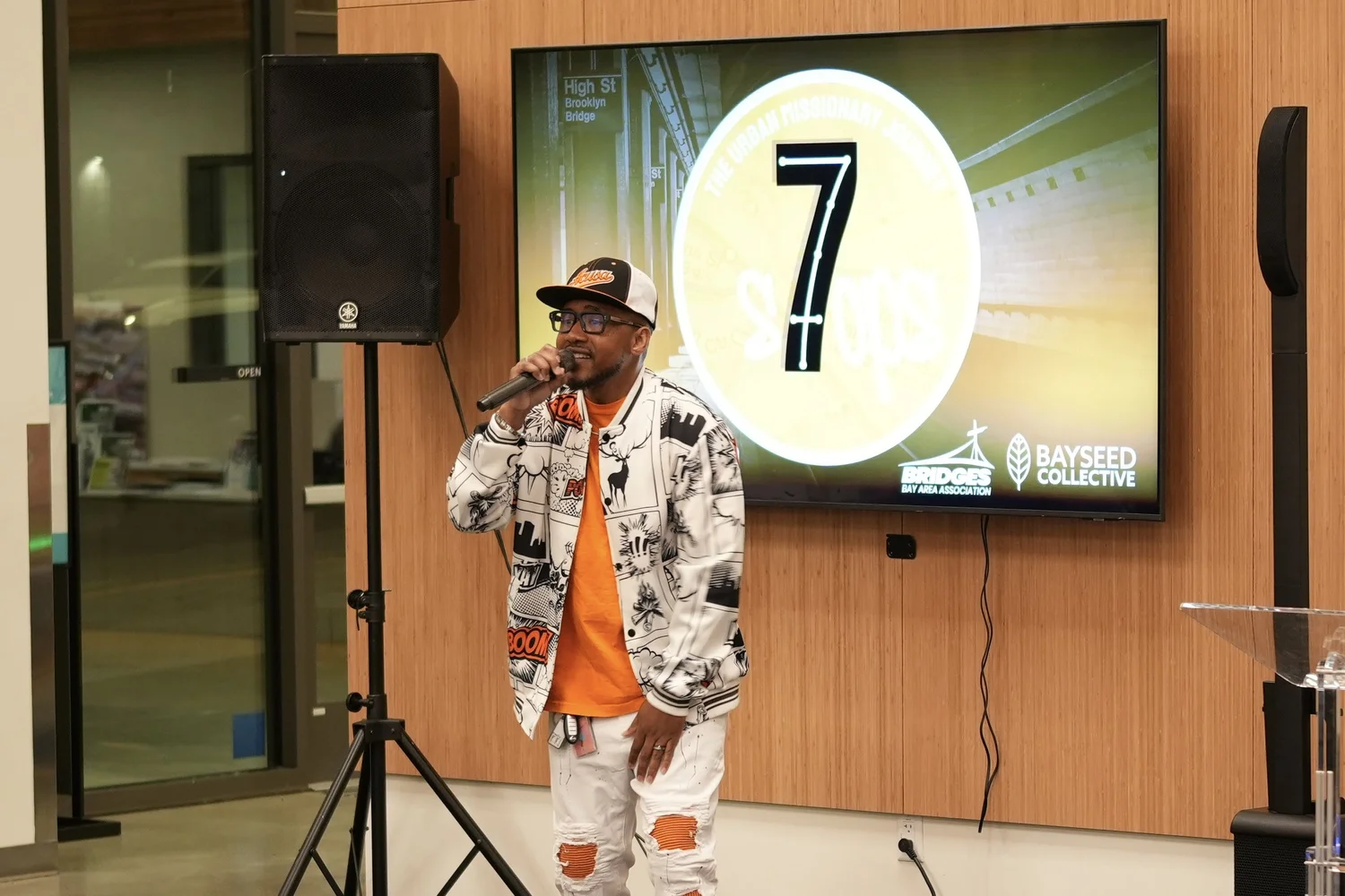 Performer in a patterned jacket beside the Seven Stops display.