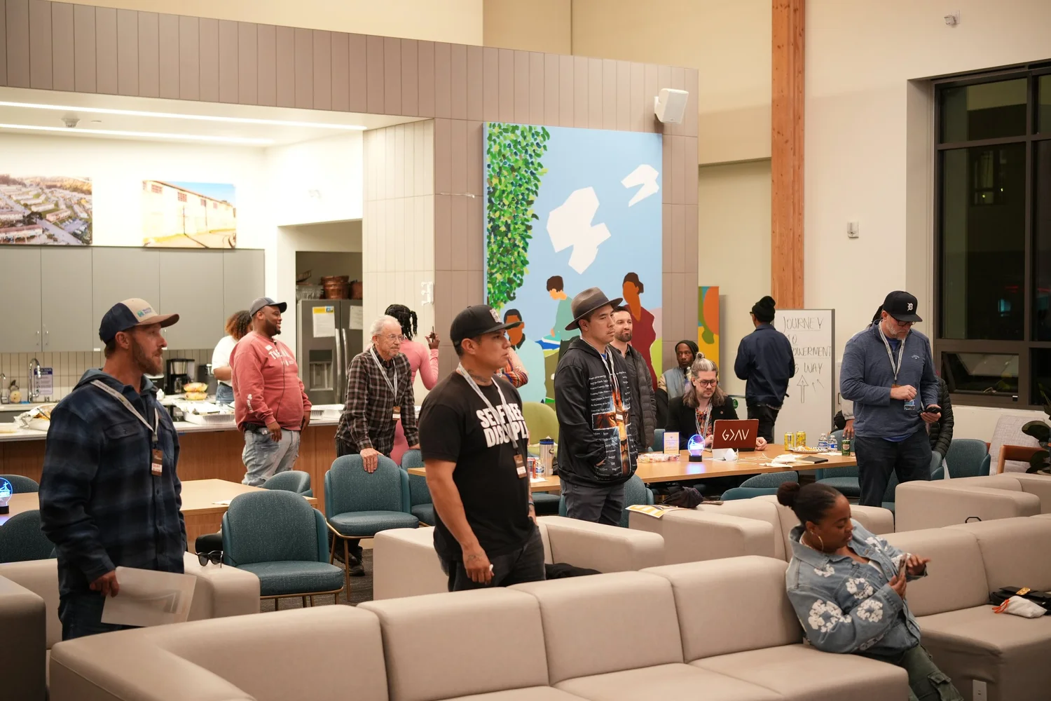 Attendees standing among sofas beneath colorful murals.