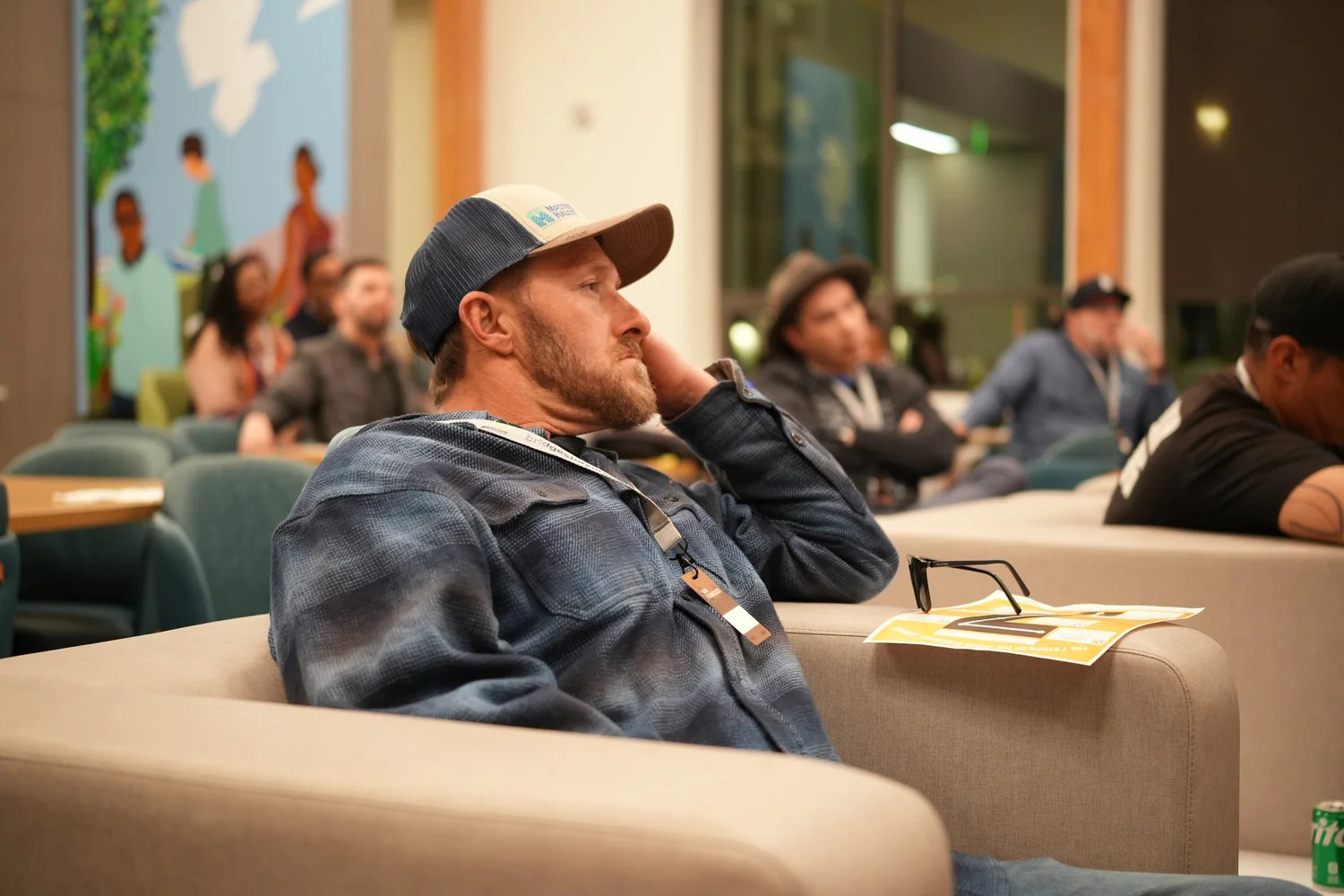 Attendee in a blue plaid shirt watching from a sofa.