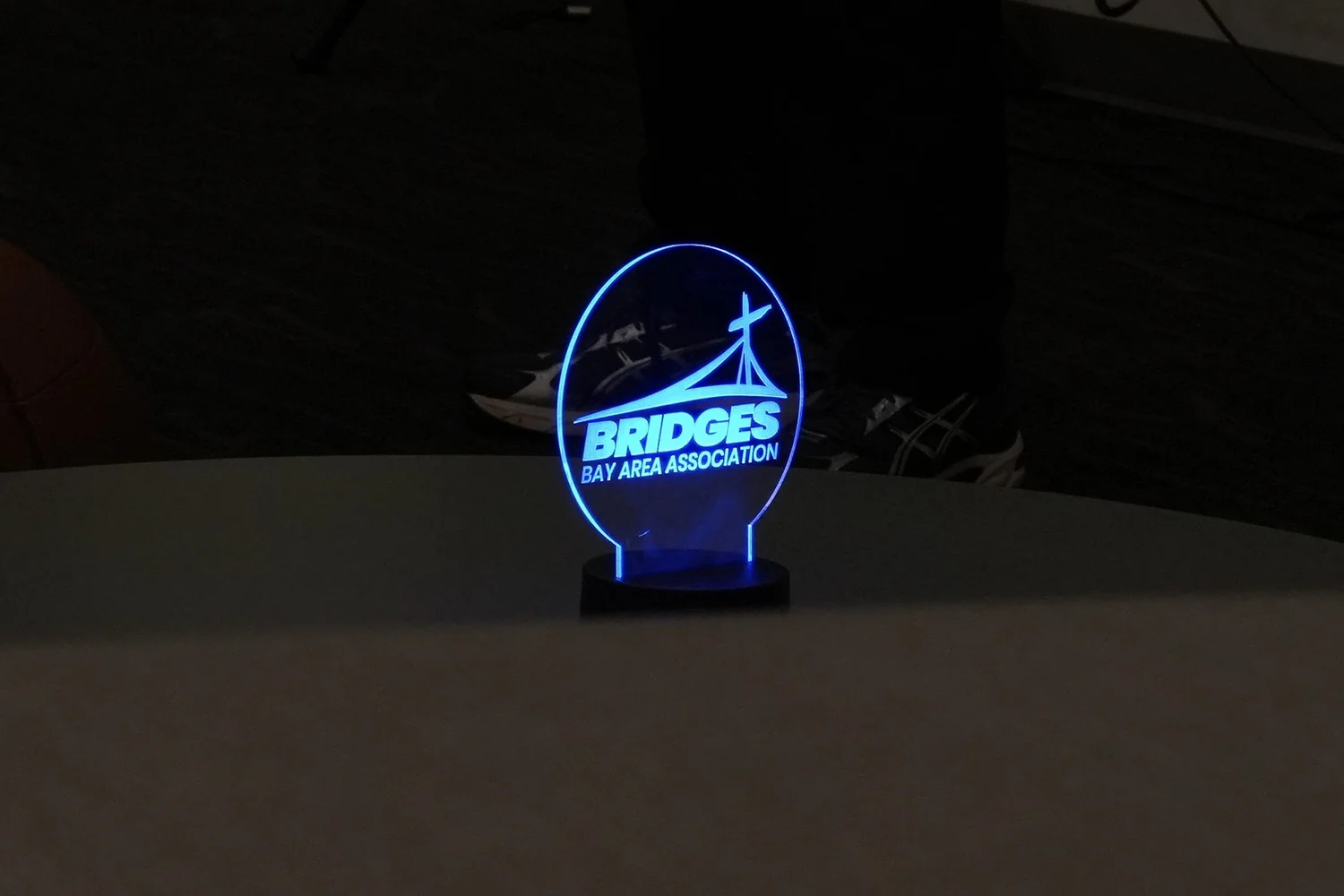 Glowing blue Bridges Bay Area Association sign against a dark background.