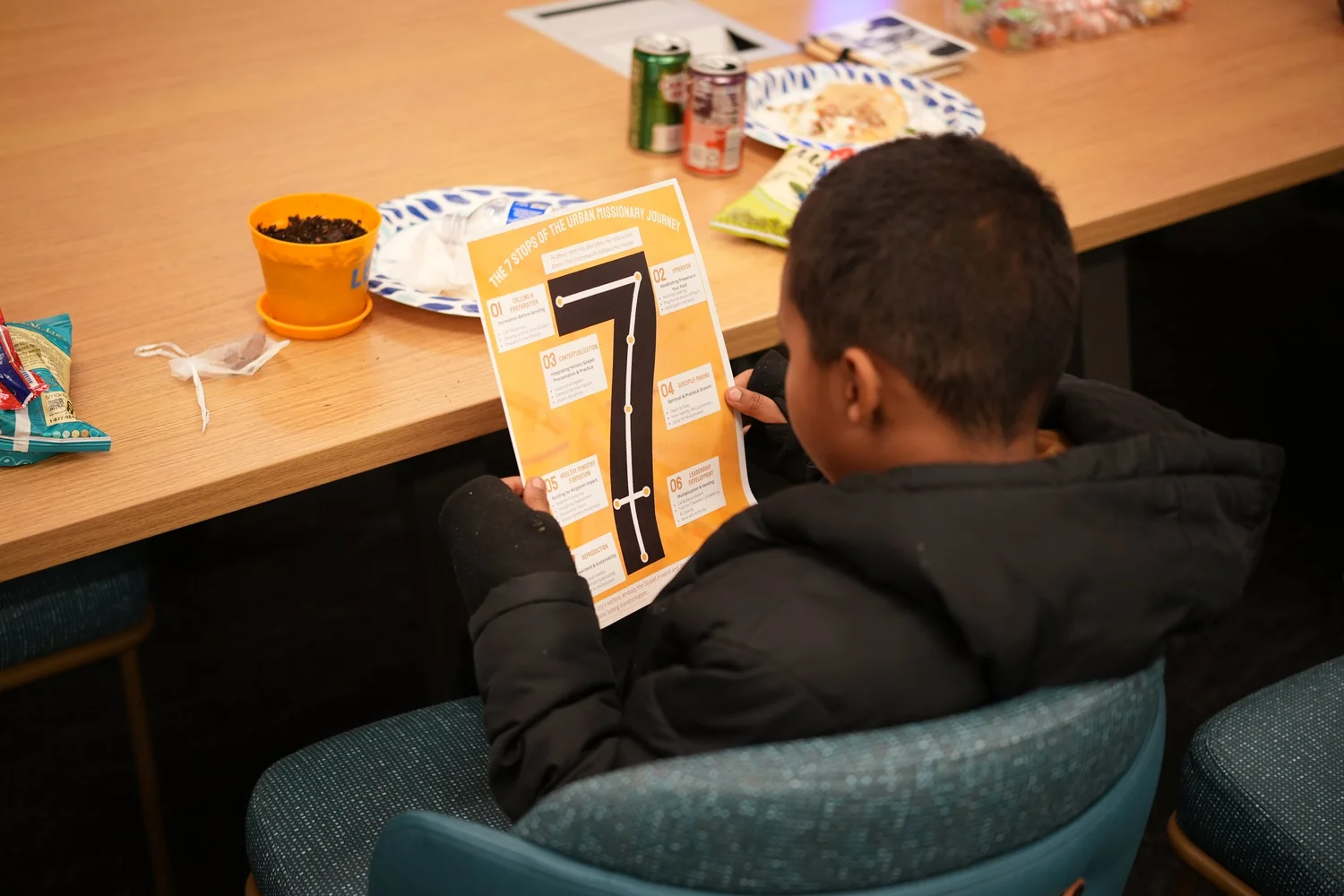 Attendee seated at a table reading a Seven Stops flyer.