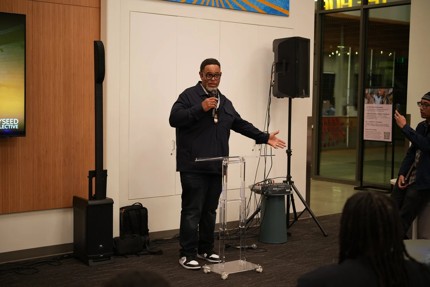 Speaker gesturing outward beside a clear lectern.