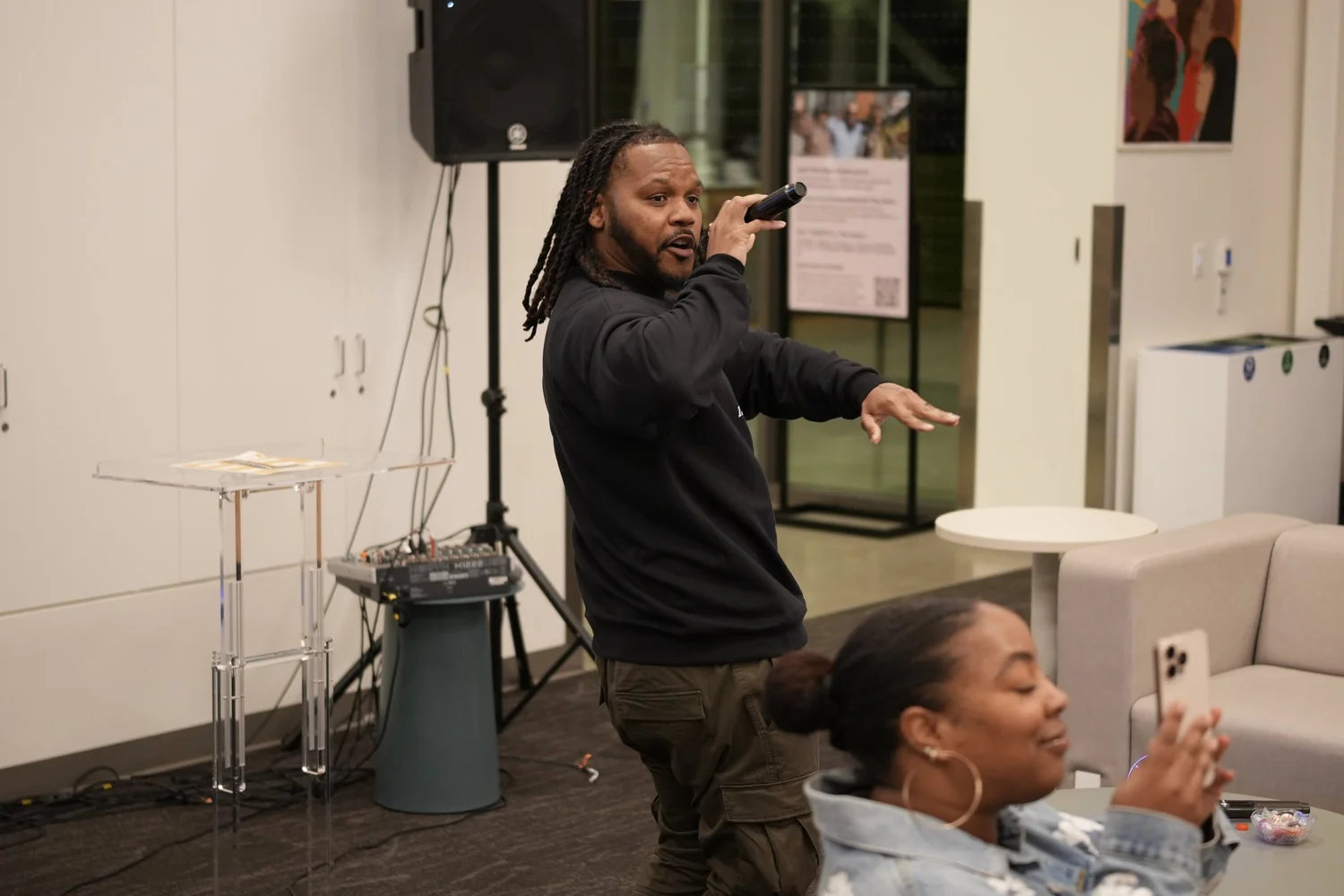 Performer gesturing toward people seated on nearby sofas.