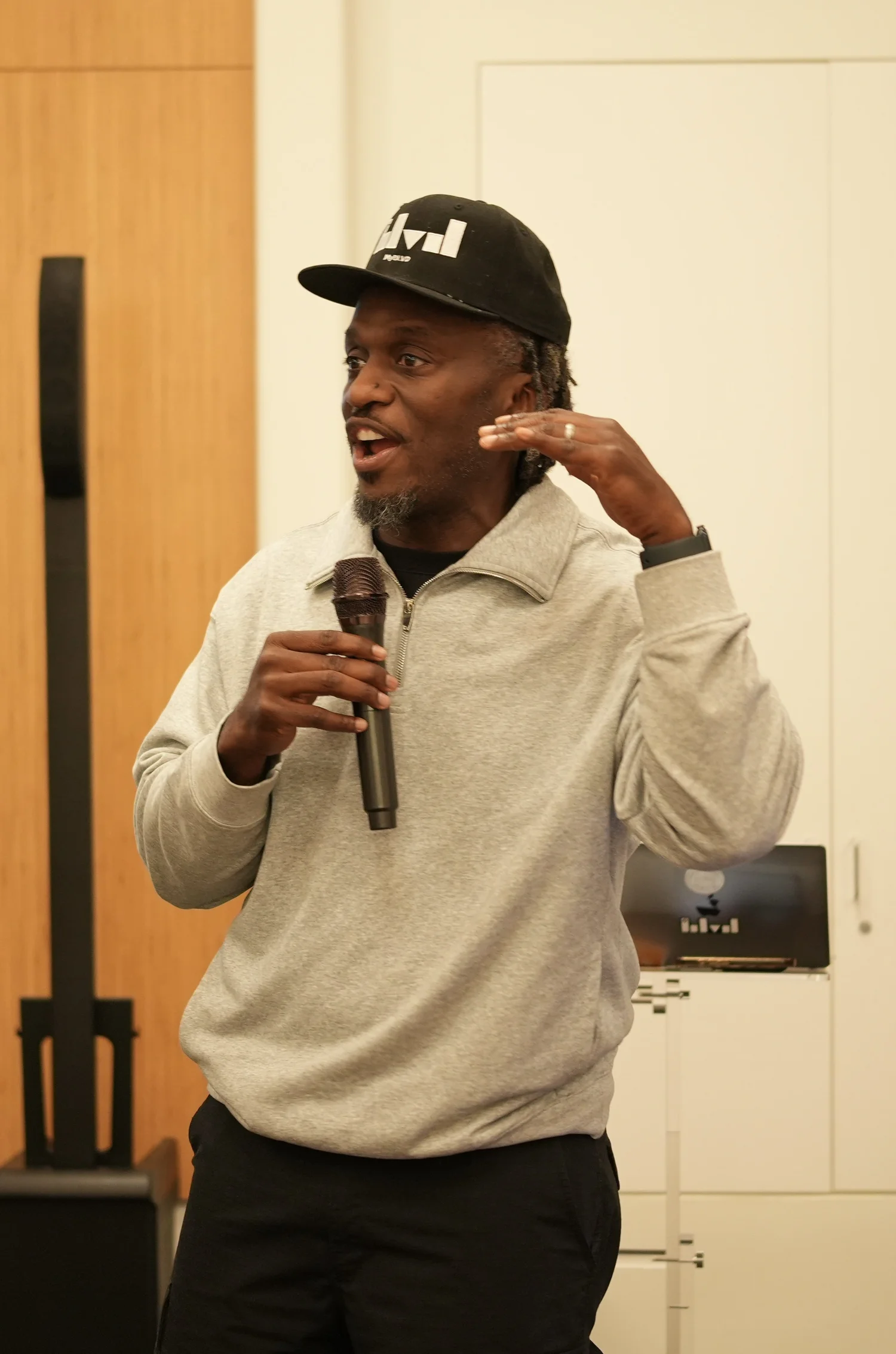 Performer in a light sweatshirt gesturing while holding a microphone.