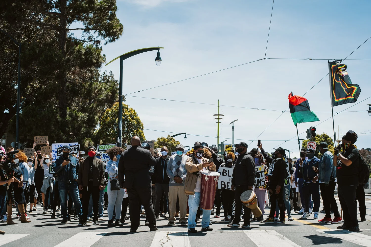 Wide view of rally participants beneath a red, black, and green flag.