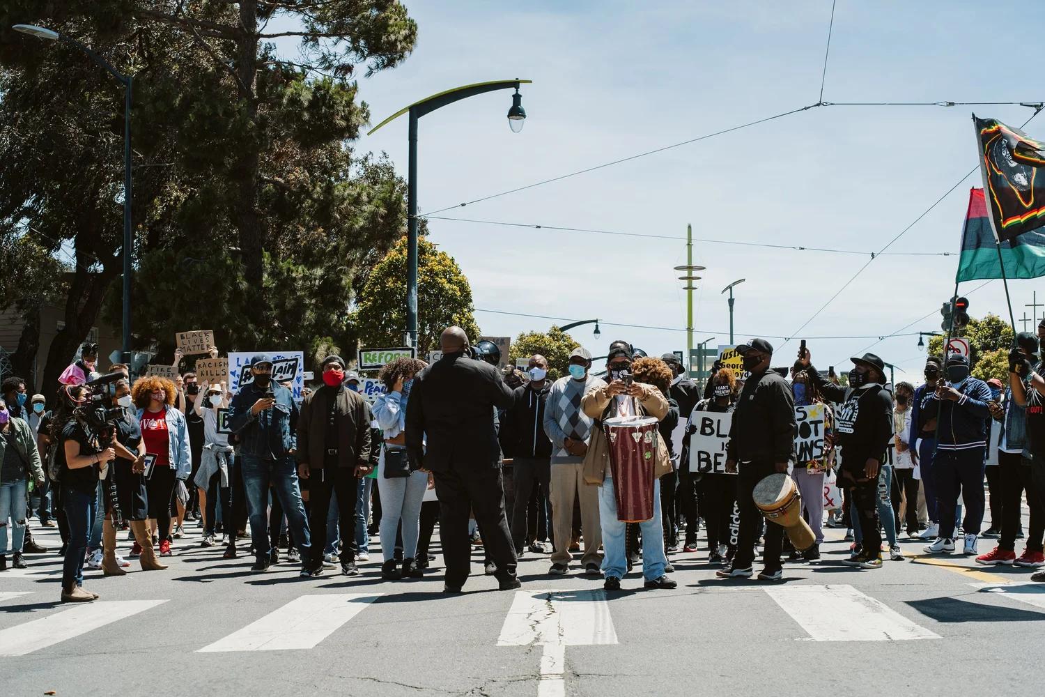 Marchers filling the street at a sunny intersection.