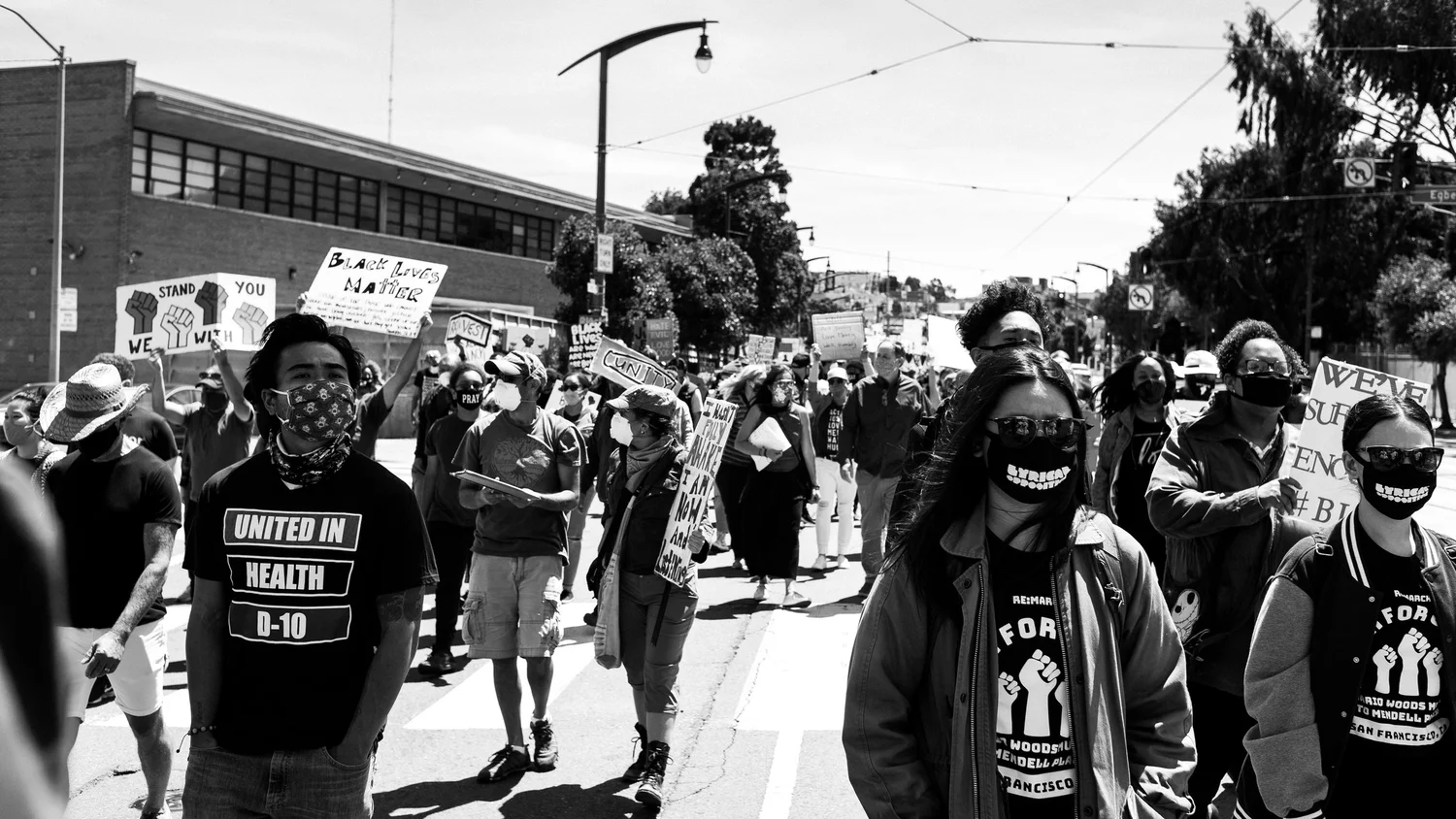 Black-and-white view of masked marchers and protest signs.