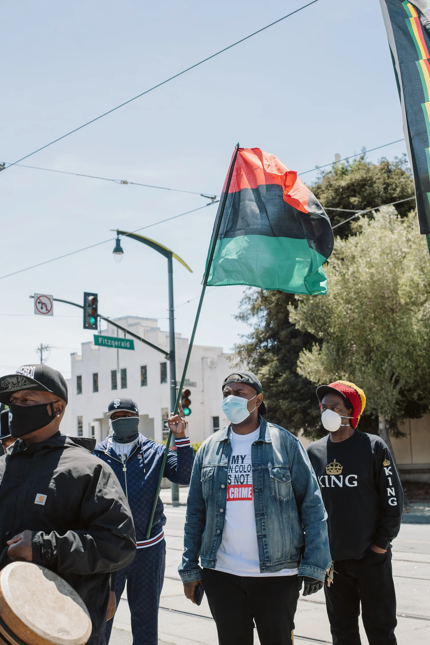 Masked participants gathered beneath overhead transit wires and a flag.