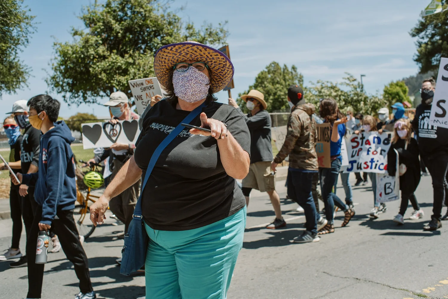 Masked marcher in a straw hat walking past the camera.