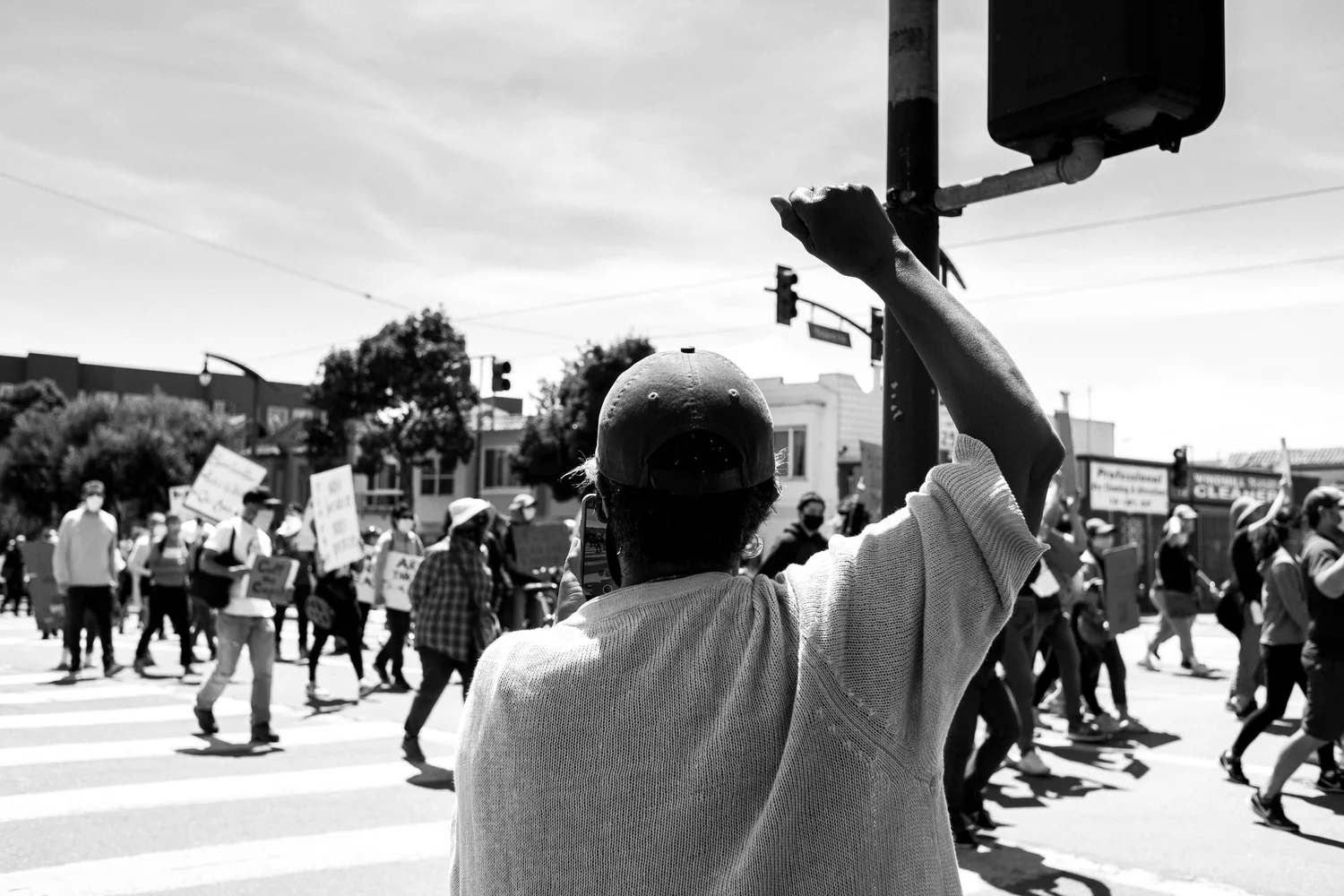 Black-and-white view of a bystander raising a fist toward marchers.