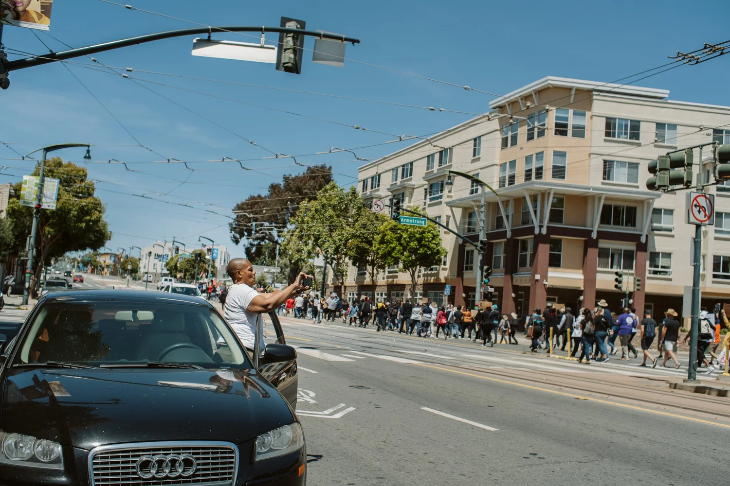 Long procession crossing an intersection beyond a parked car.