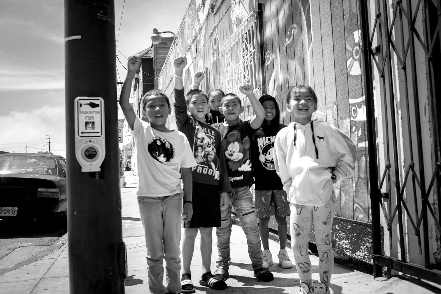 Black-and-white photo of children raising their fists beside a mural.