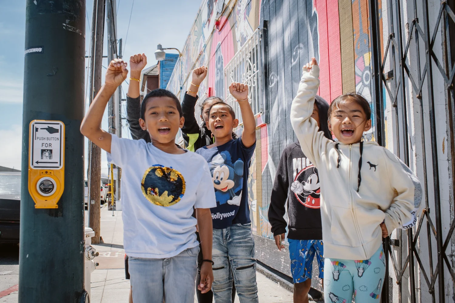 Children raising their fists beside a painted storefront.