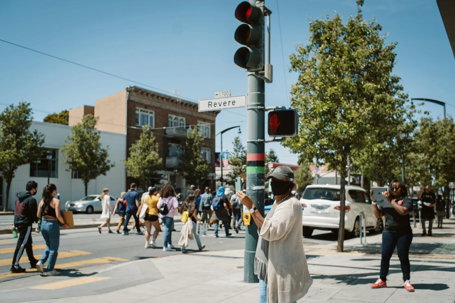 People watching marchers cross a sunny intersection.