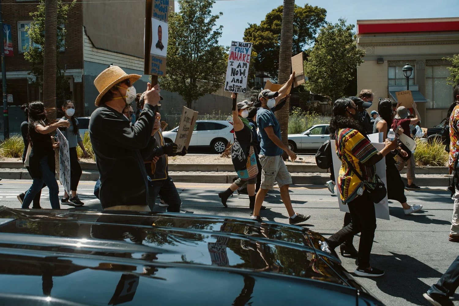 Marchers carrying signs past a parked car.