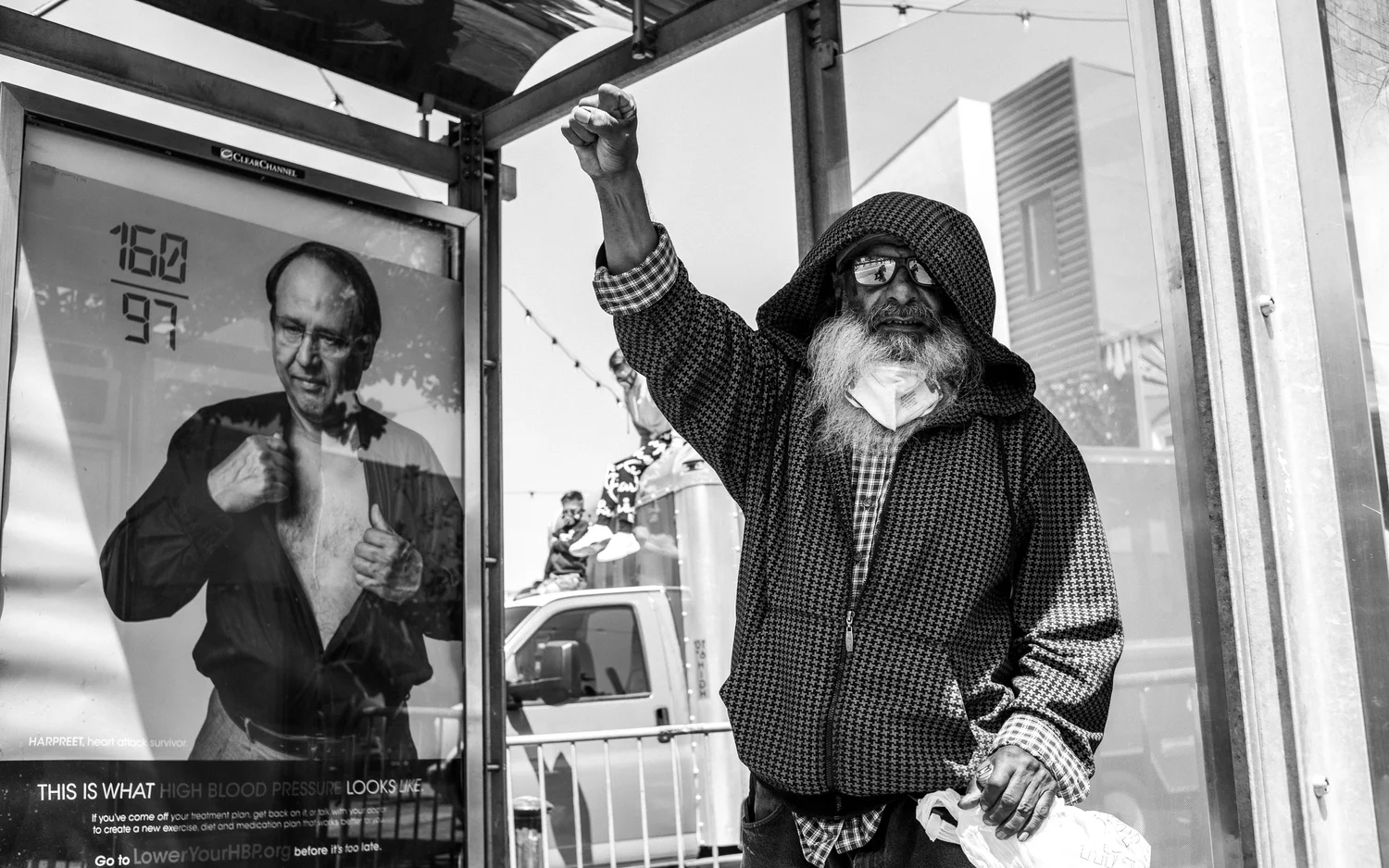 Black-and-white photo of a bearded bystander raising a fist at a transit shelter.