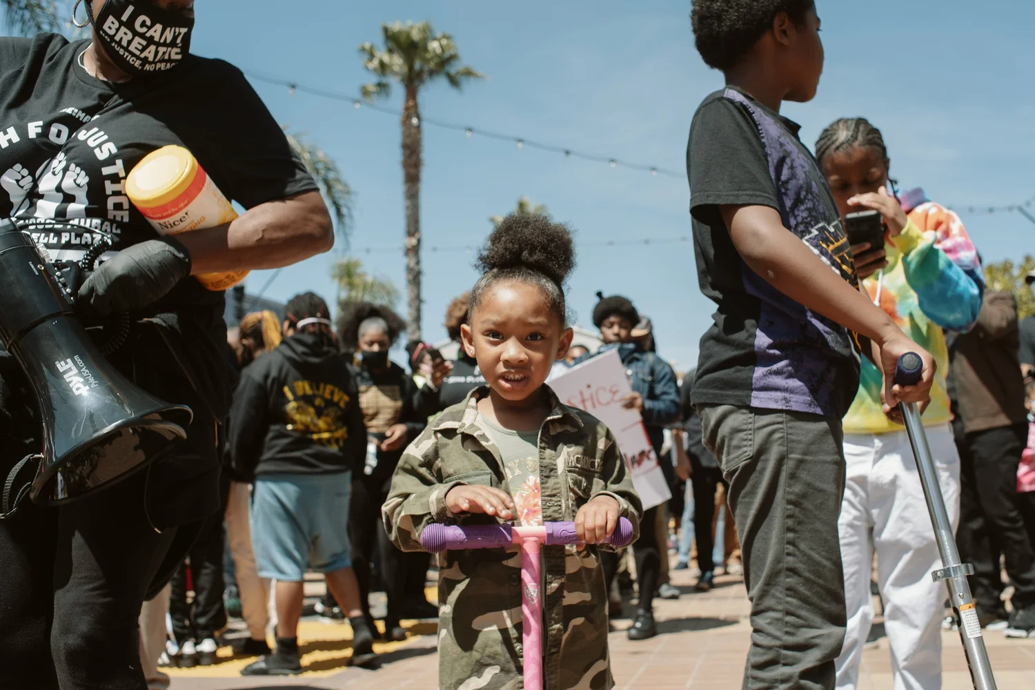 Child holding a purple scooter among rally participants.