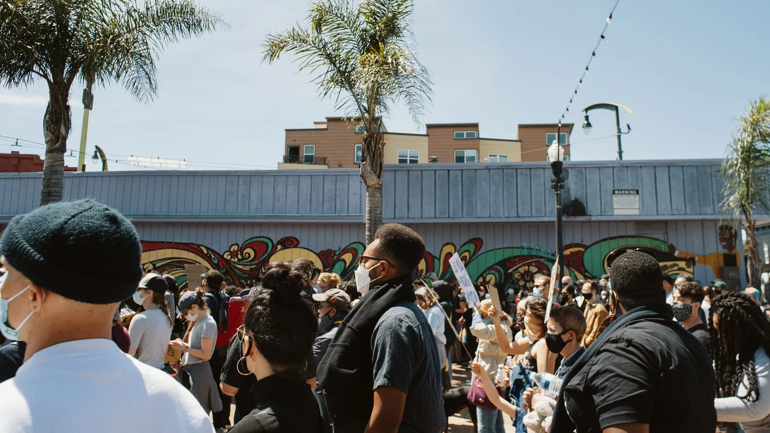Crowd listening beneath palm trees.