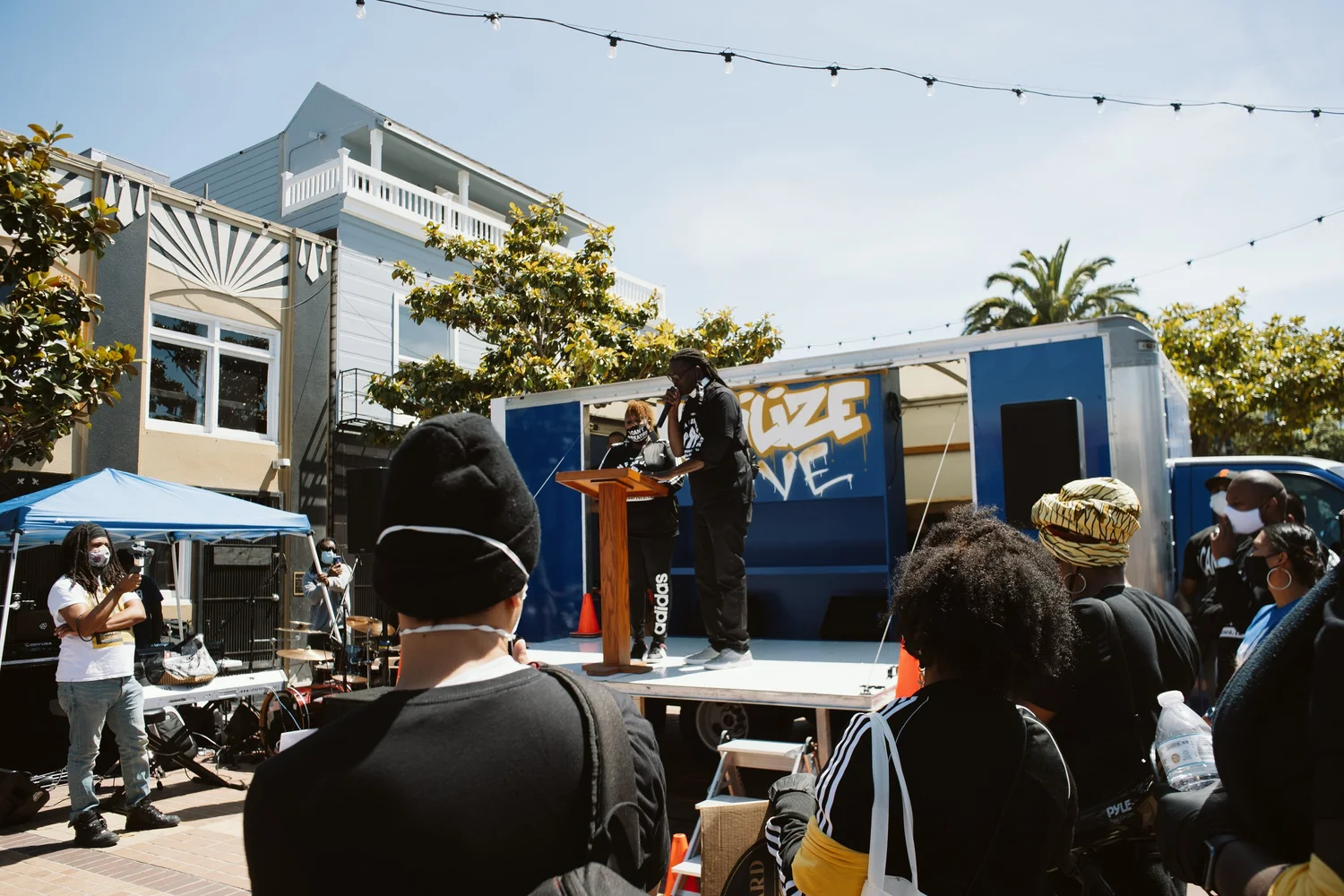 Attendees watching a speaker beside a blue stage truck.