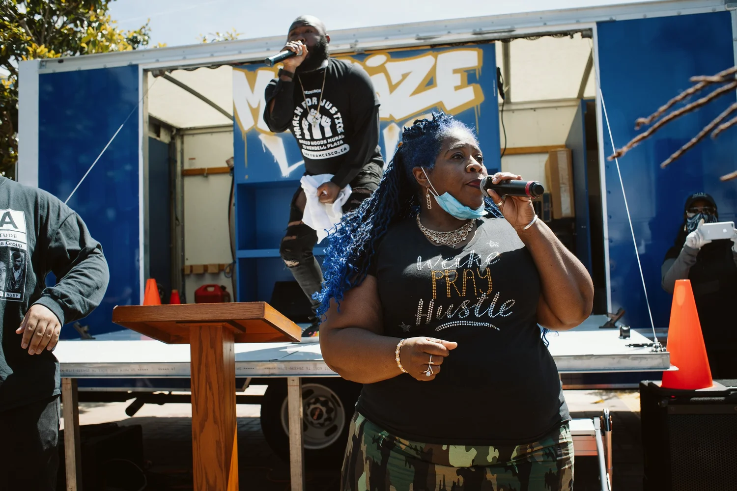 Speaker holding a microphone in front of the blue stage truck.