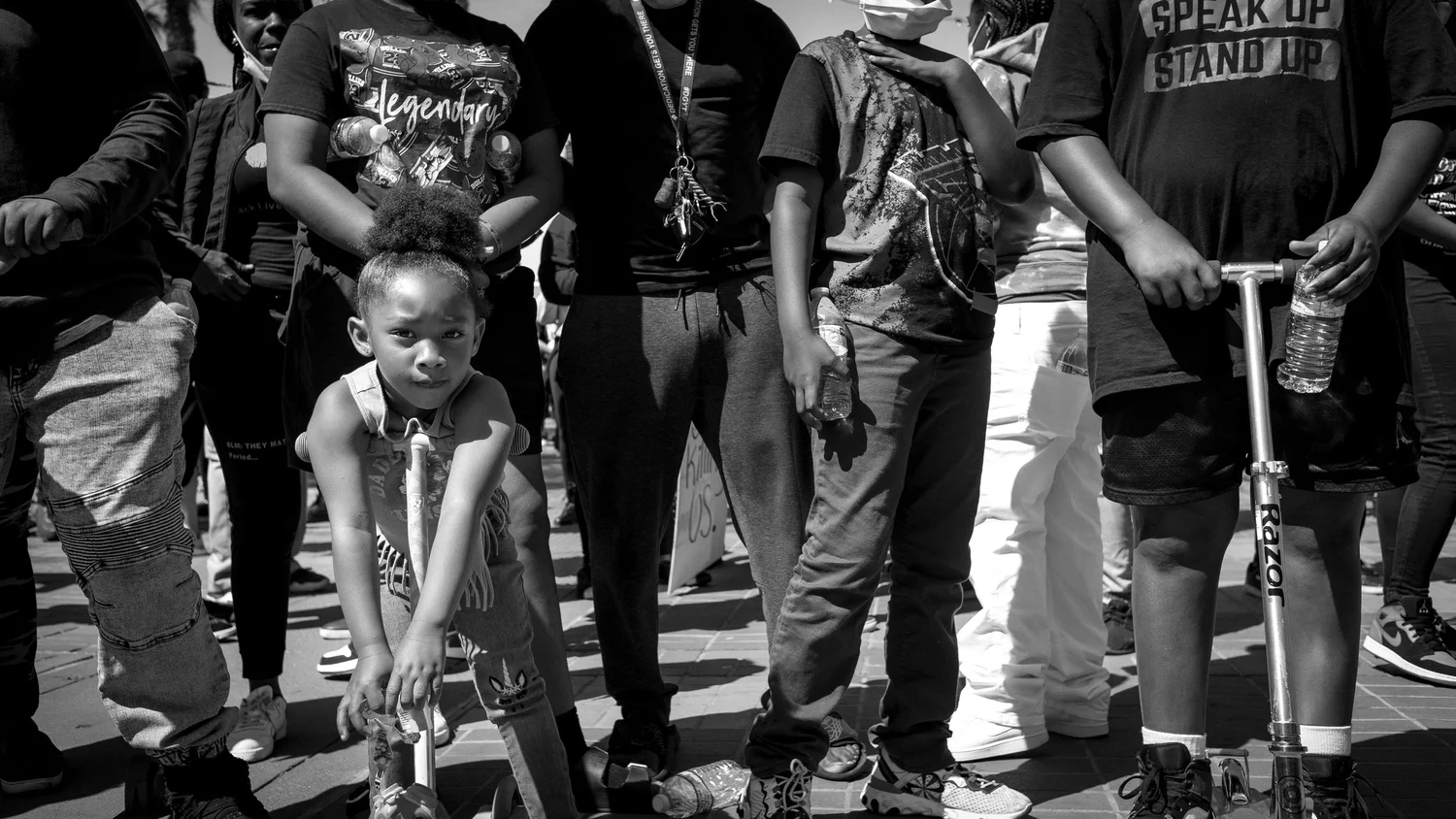 Black-and-white photo of a child with a scooter among adults.