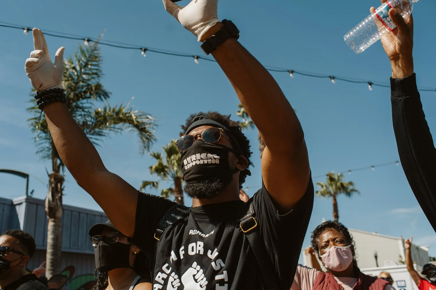 Masked participant raising both arms and holding a phone.