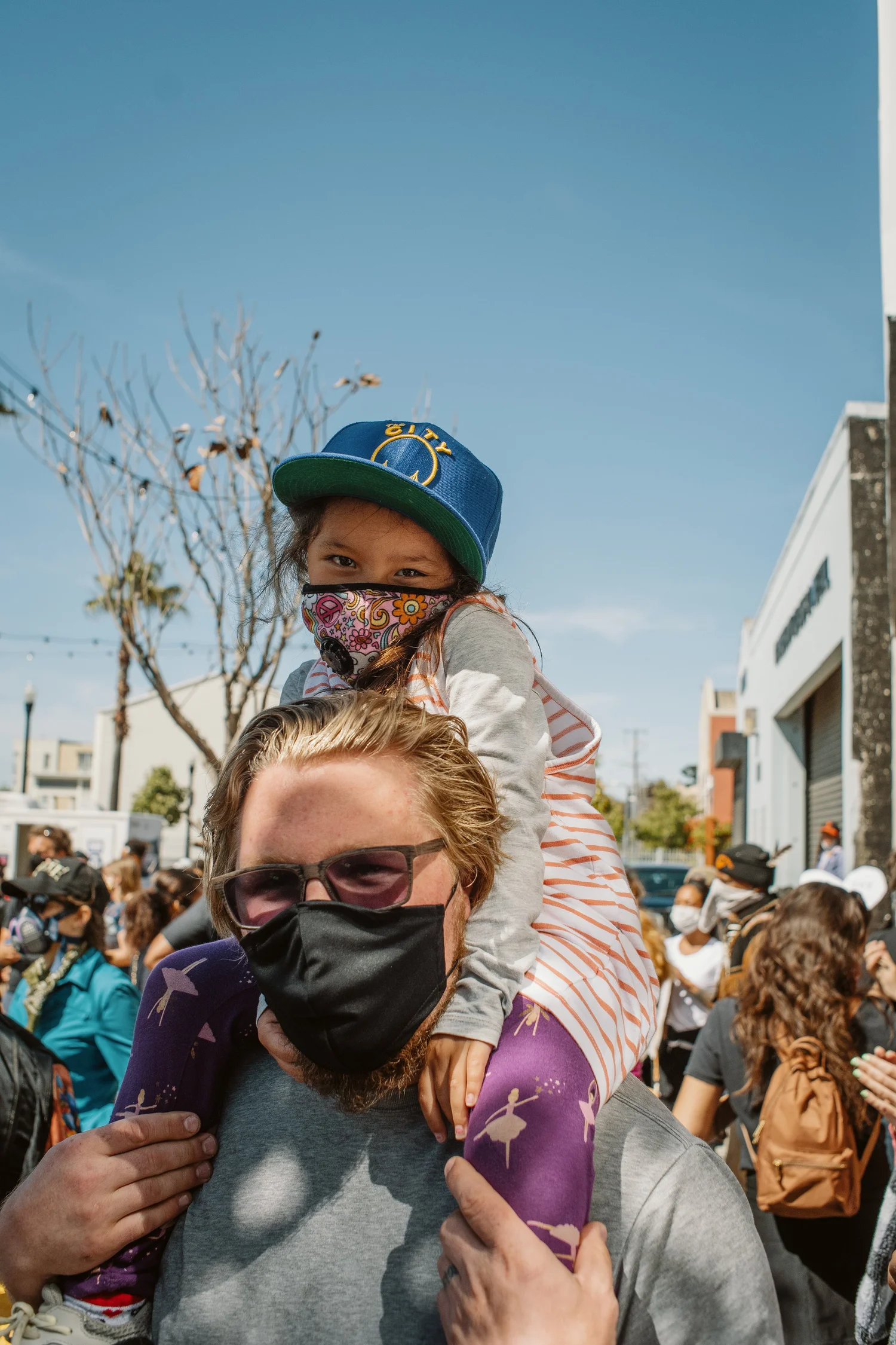 Masked adult carrying a child on their shoulders.