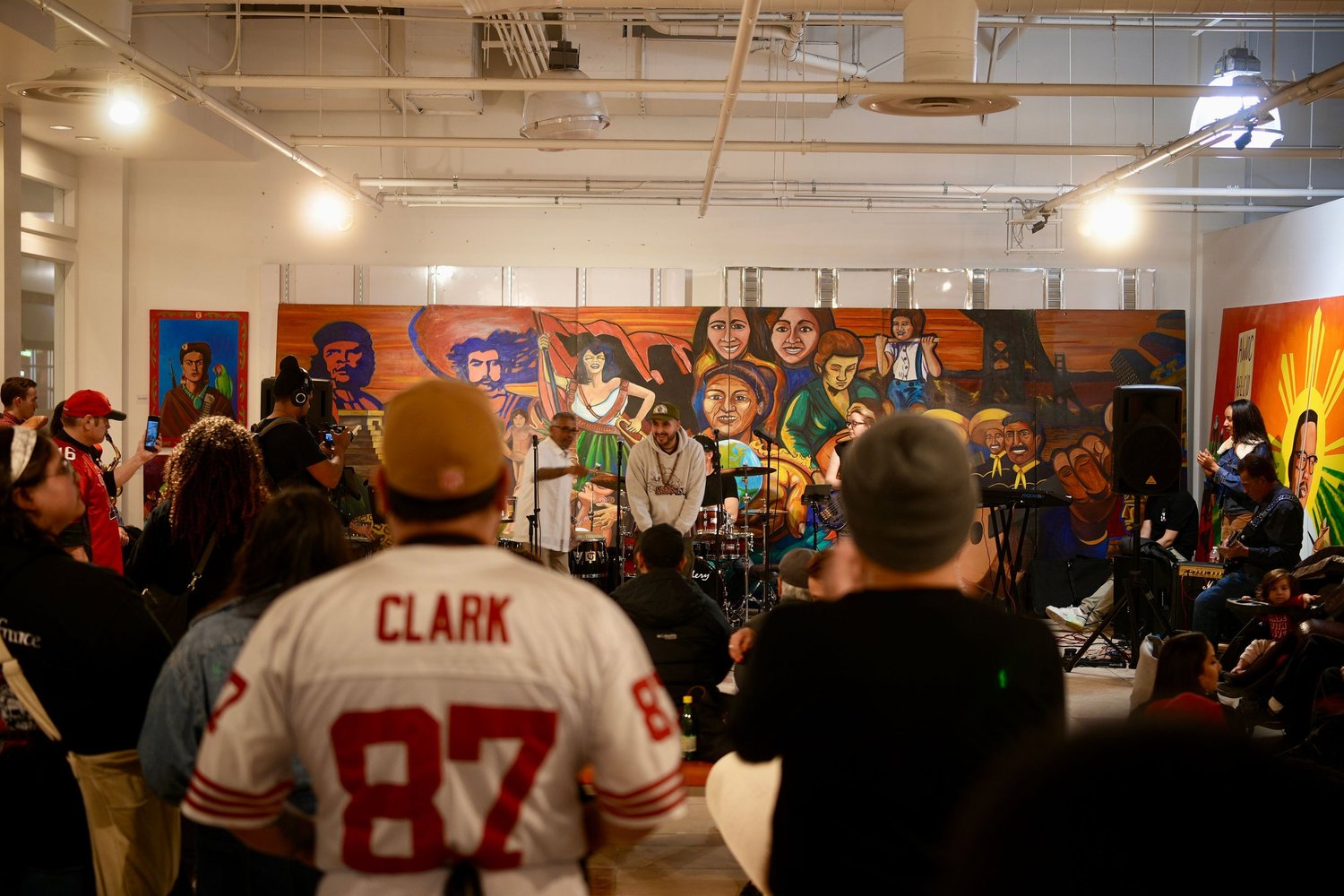 Audience members watch a band perform in front of a mural.