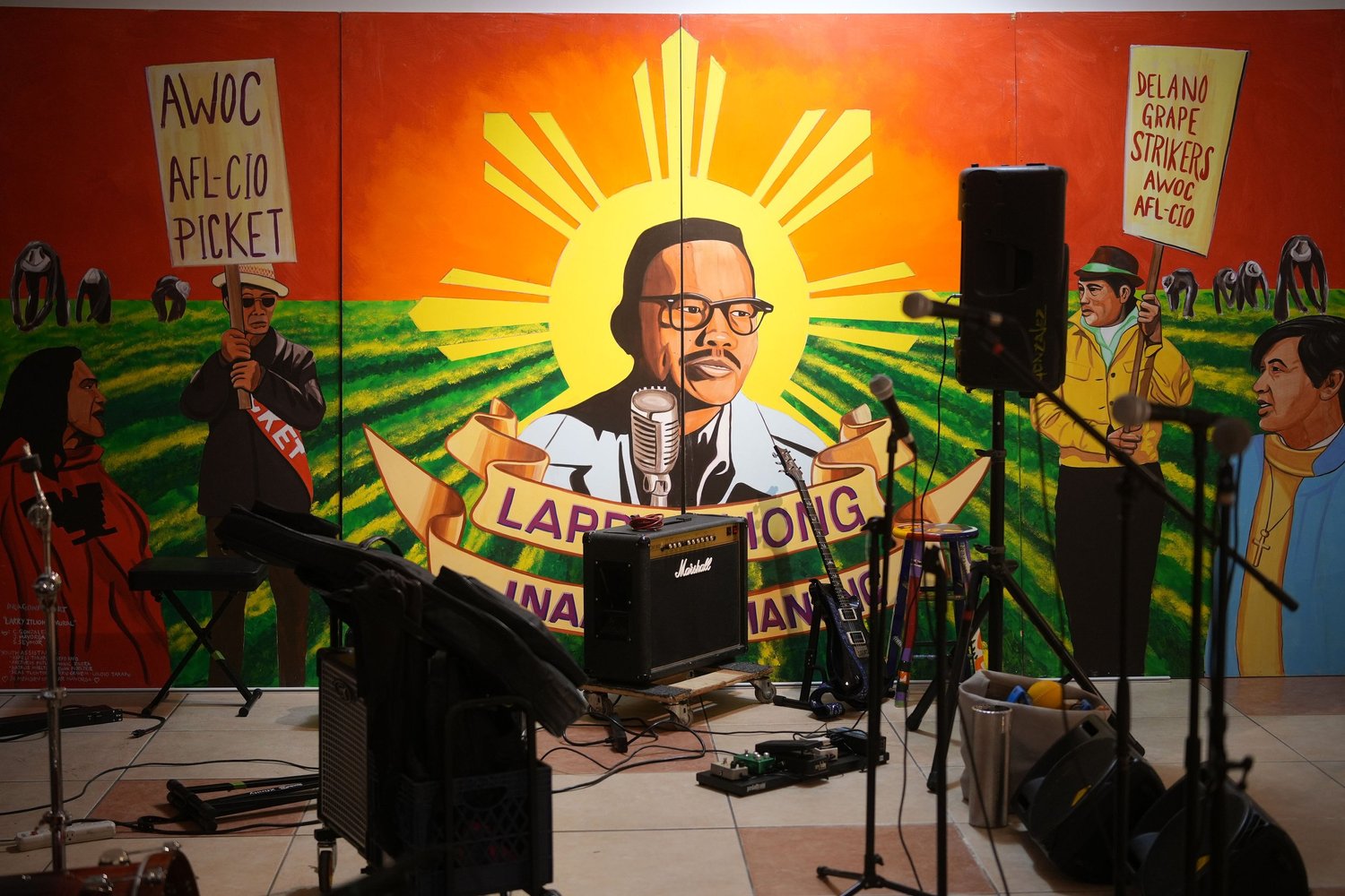 A DJ performs in front of a mural featuring Larry Itliong.