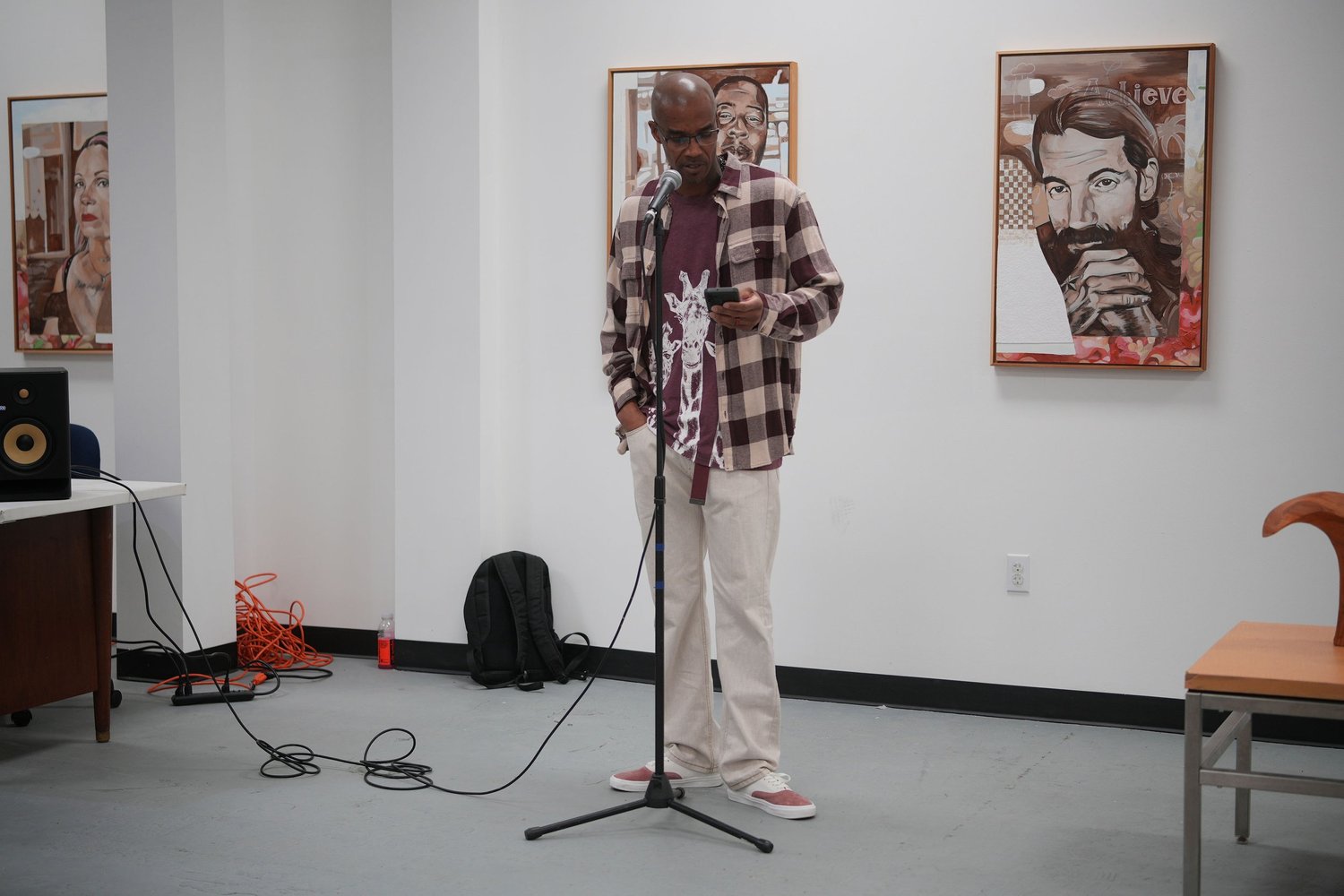 A speaker stands at a microphone between framed portraits.