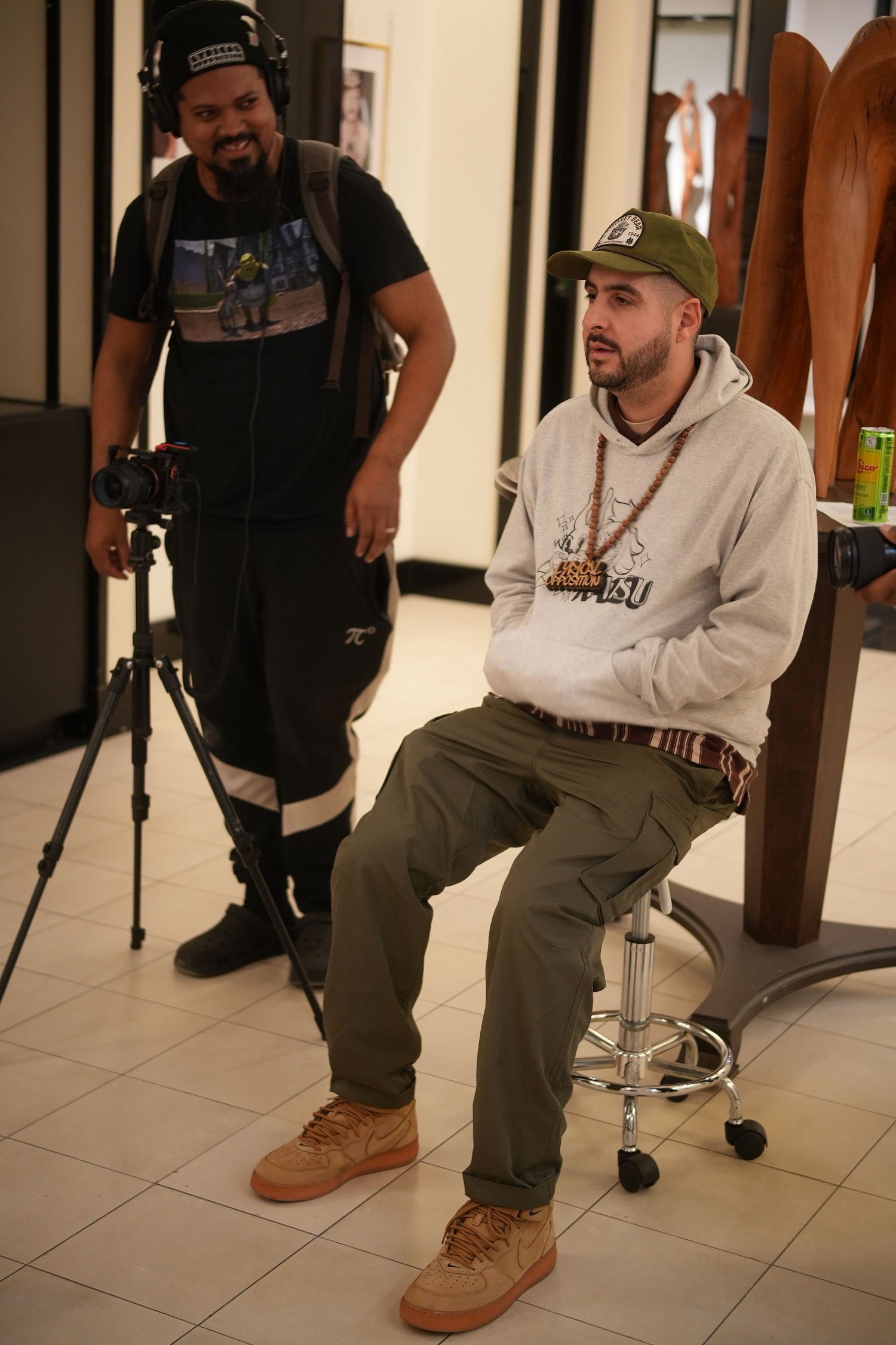 Two participants sit and stand beside recording equipment.