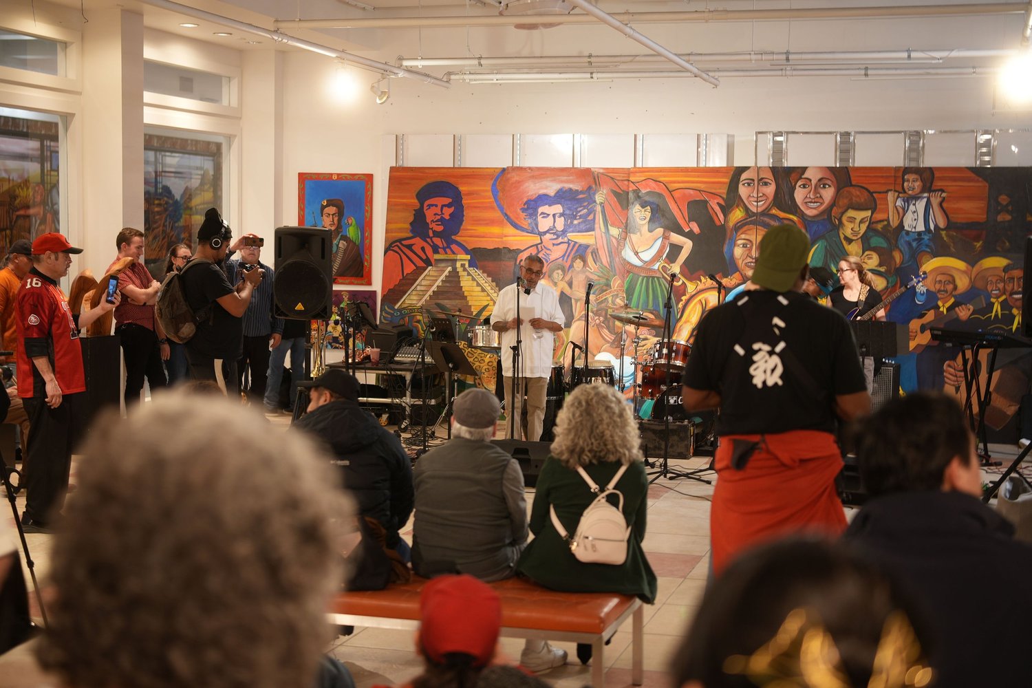 The audience watches vocalists perform in front of the mural.
