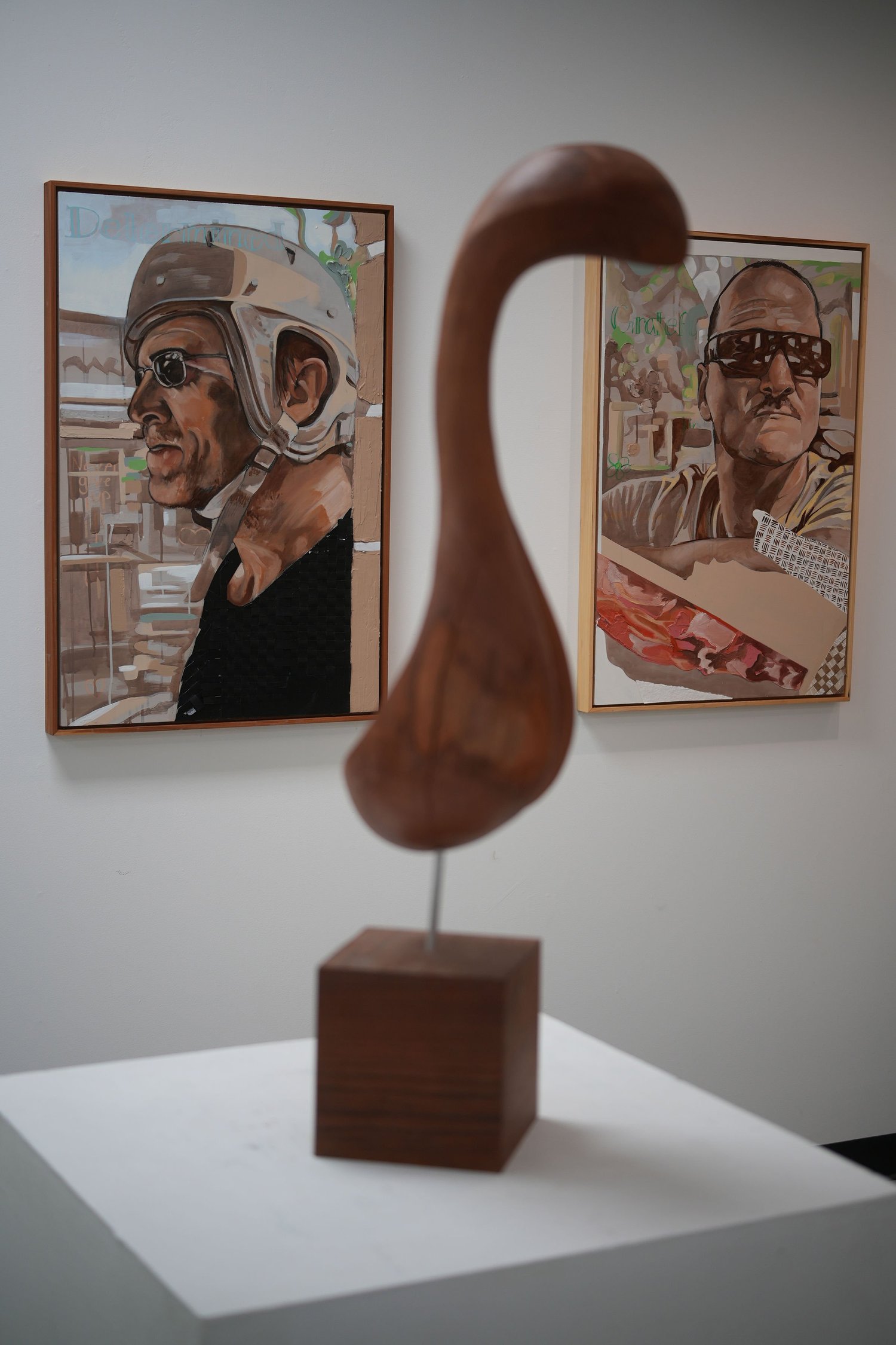 A curved wooden sculpture displayed between framed portraits.
