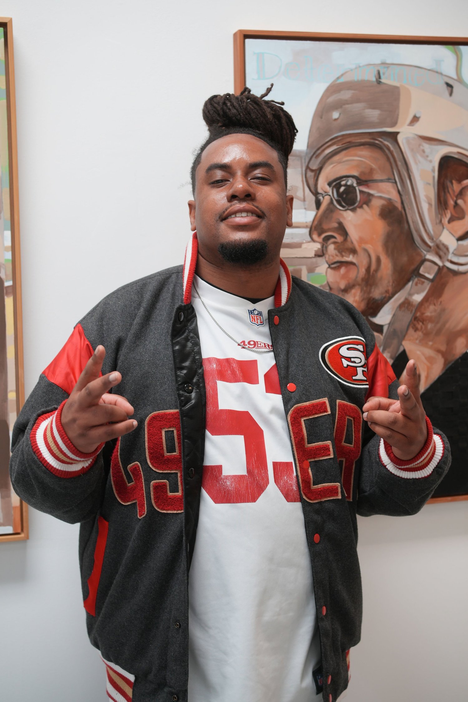 A visitor in a football jersey poses beside artwork.