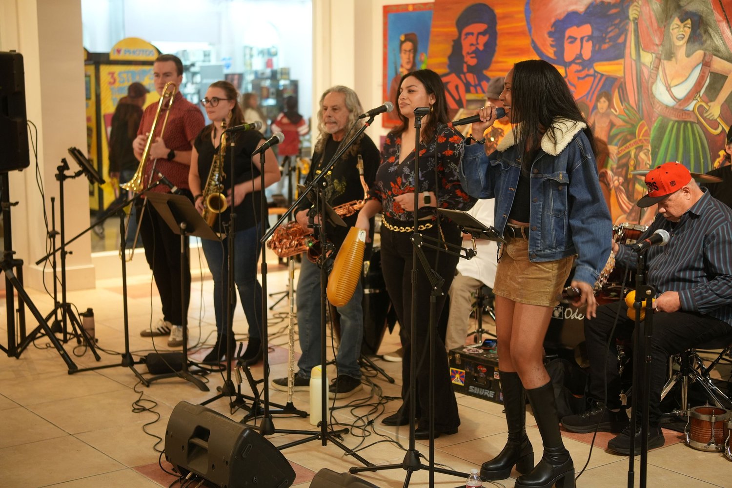 Vocalists and instrumentalists perform before an audience and a colorful mural.