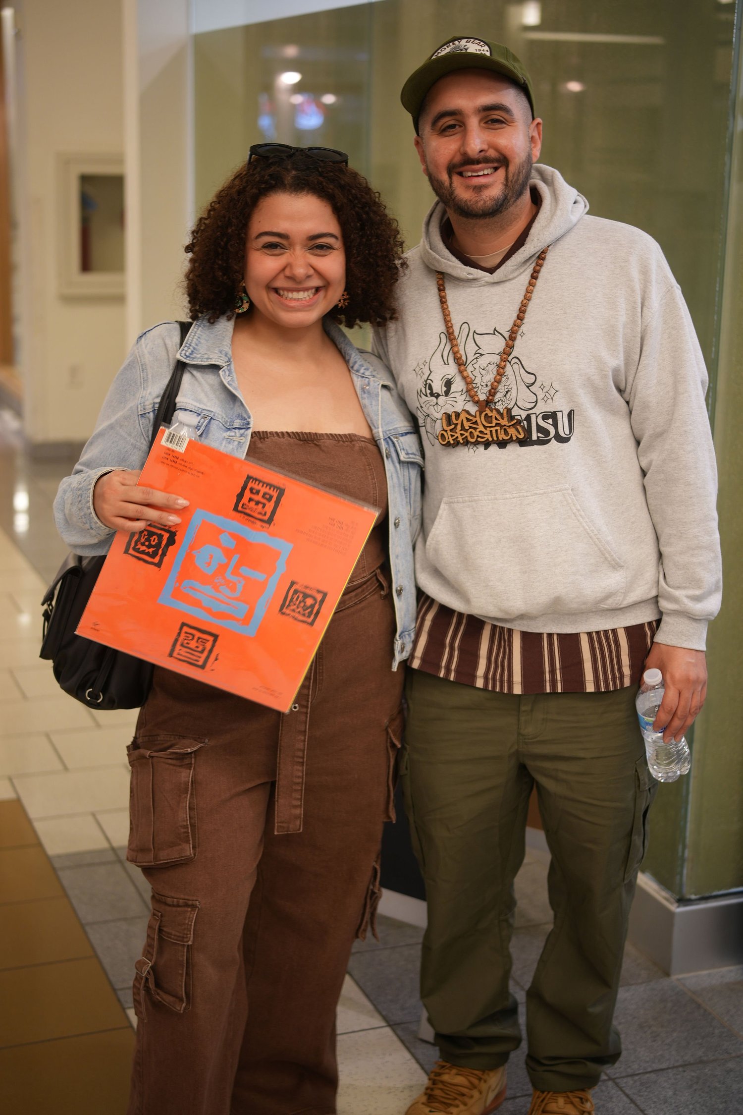 Two guests pose together, one holding a colorful print.