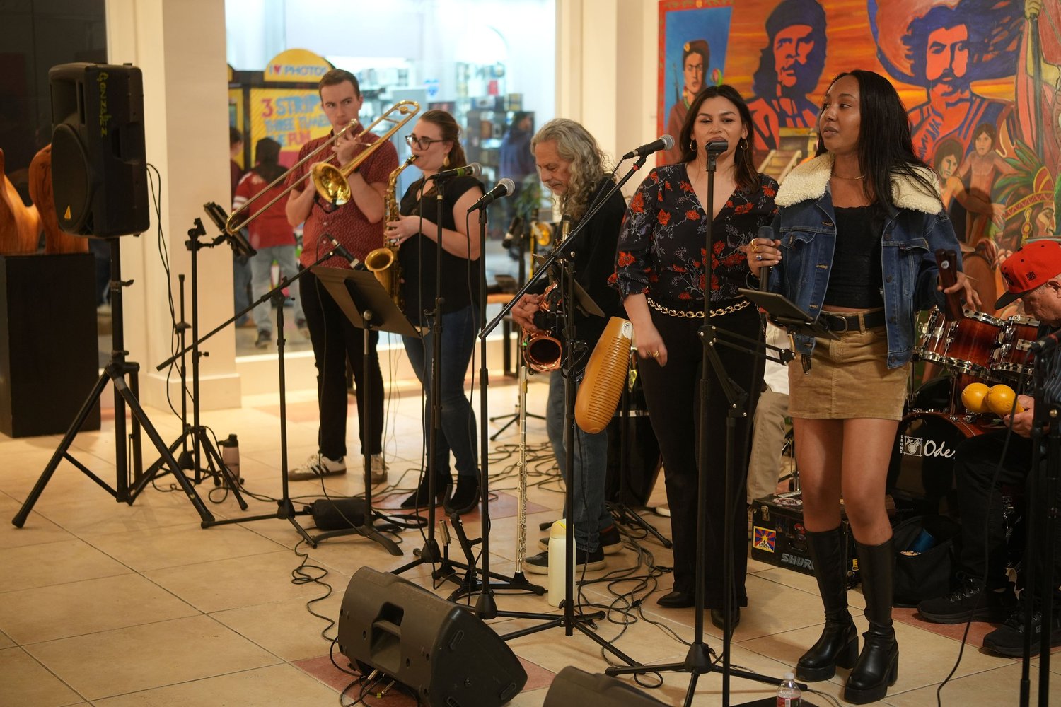 Vocalists and instrumentalists perform before an audience and a colorful mural.
