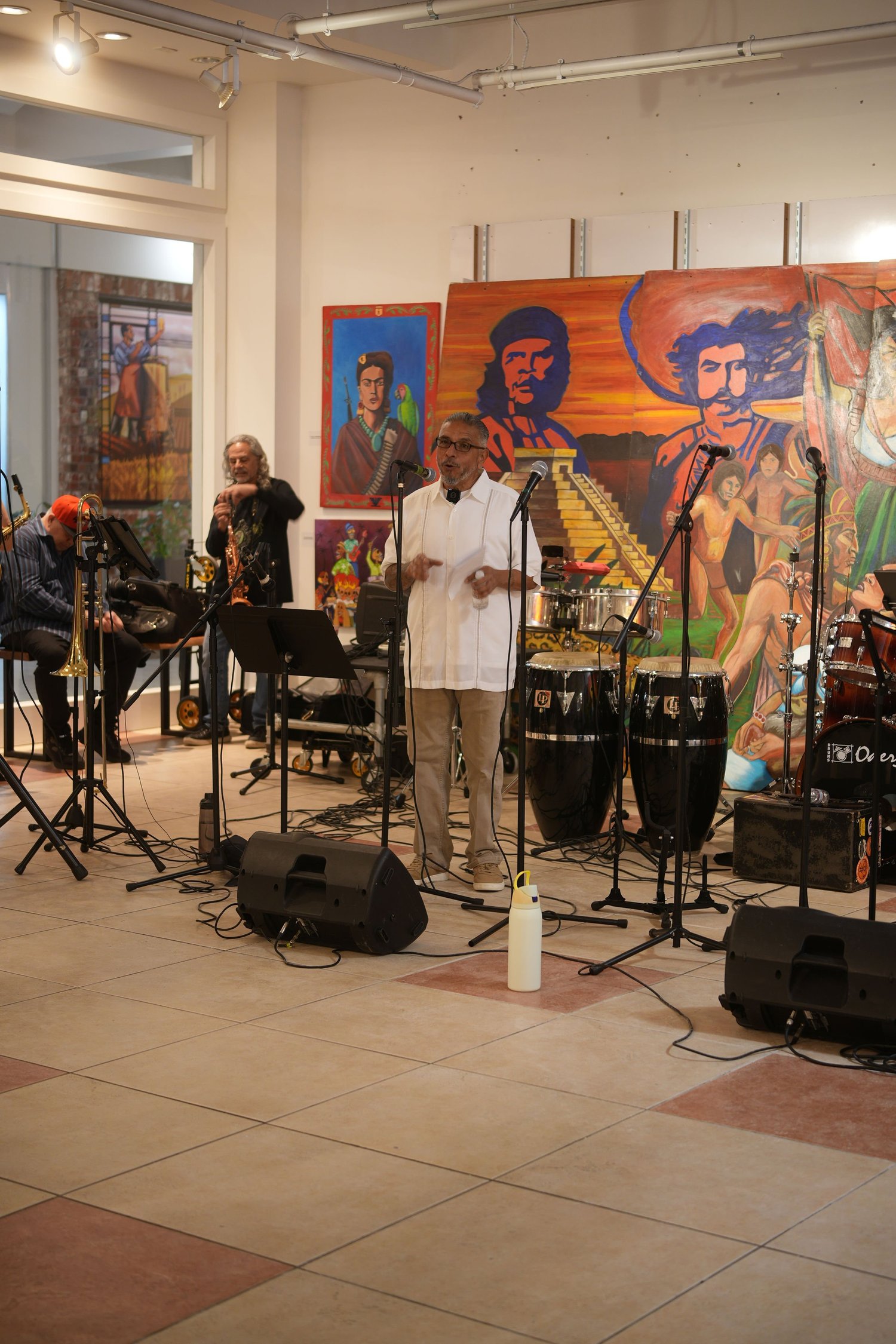 Vocalists and instrumentalists perform before an audience and a colorful mural.