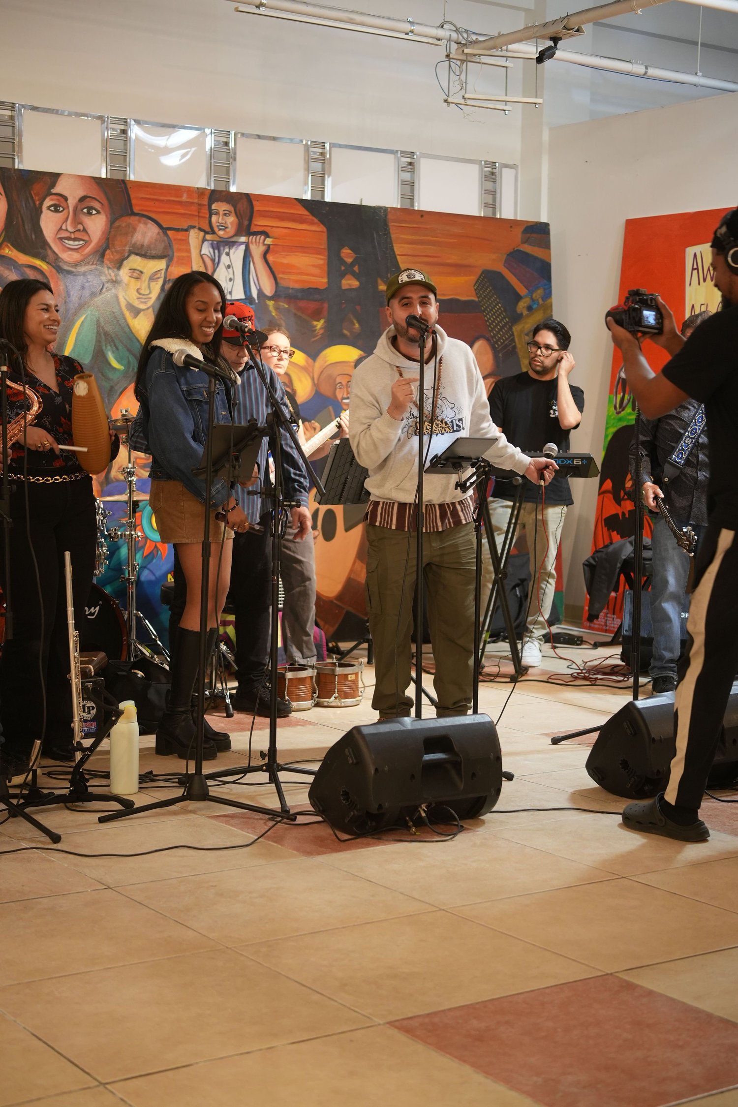 Vocalists and instrumentalists perform before an audience and a colorful mural.