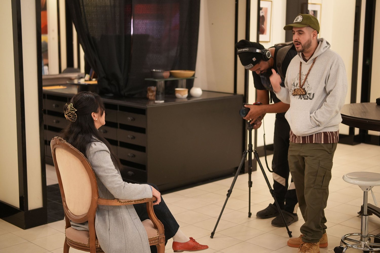 An interviewer and participant converse beside framed artwork.