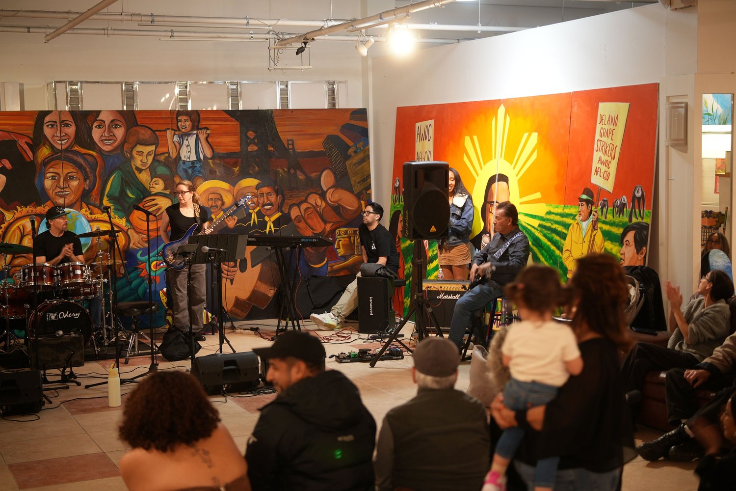 Vocalists and instrumentalists perform before an audience and a colorful mural.