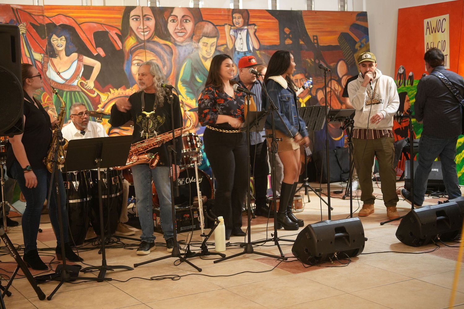 Vocalists and instrumentalists perform before an audience and a colorful mural.