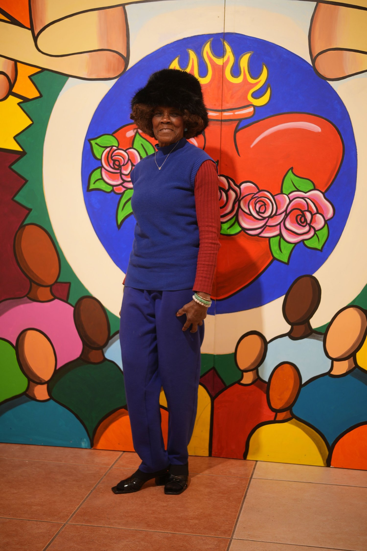 A visitor poses in front of a colorful heart mural.