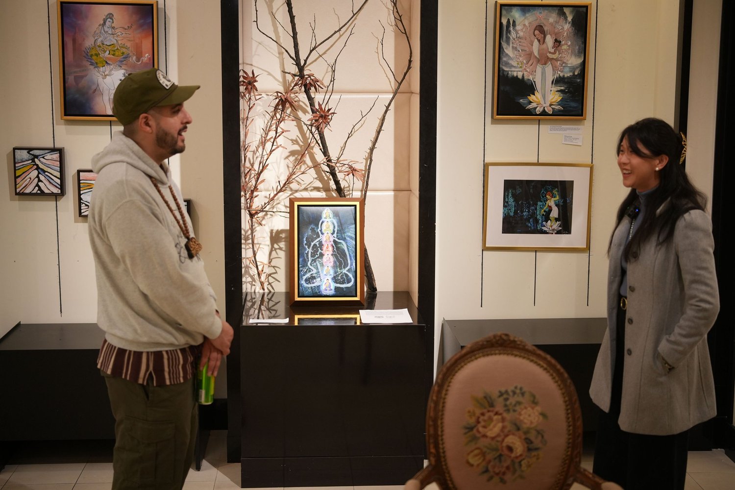An interviewer and participant converse beside framed artwork.