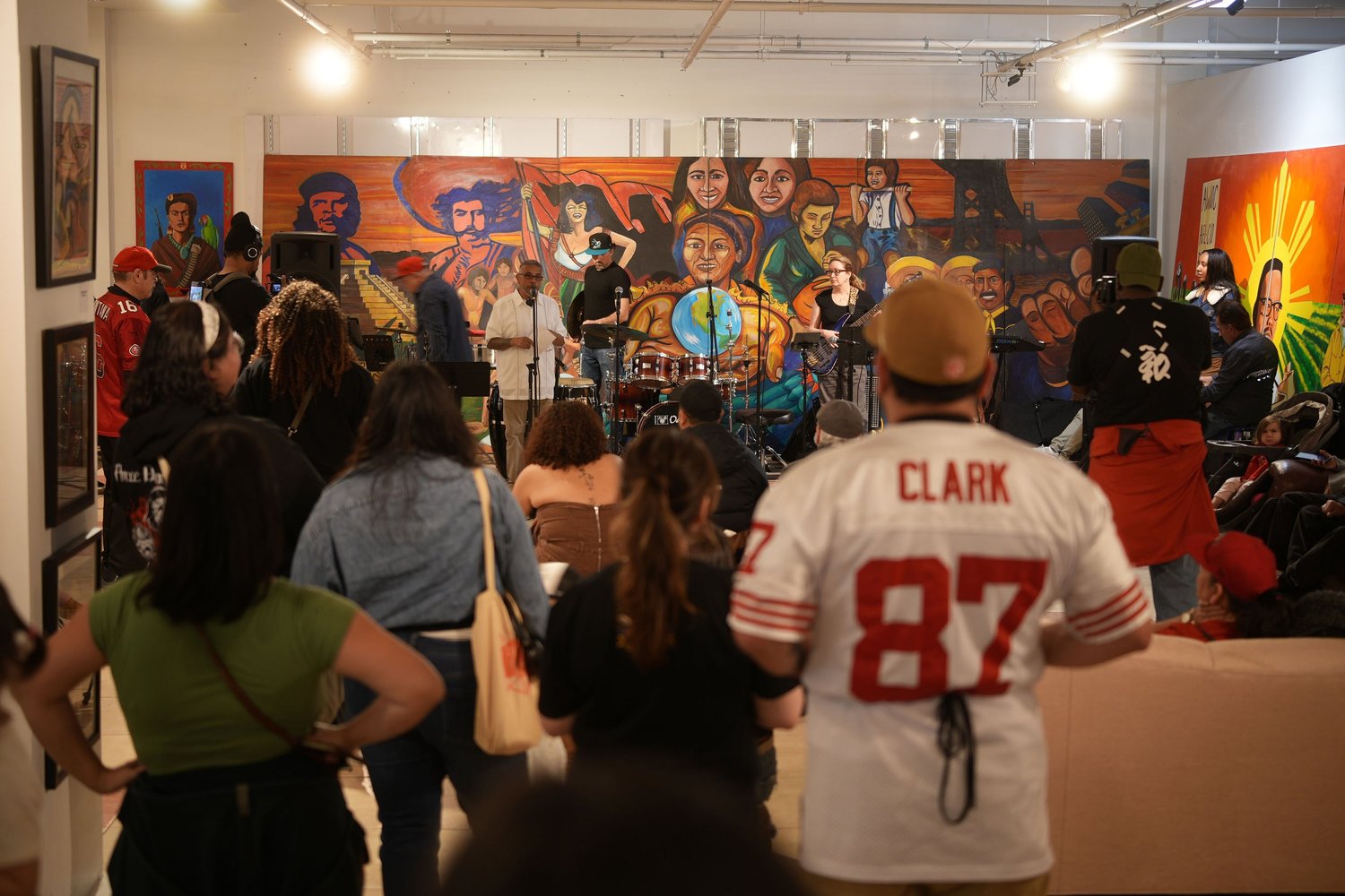 Vocalists and instrumentalists perform before an audience and a colorful mural.